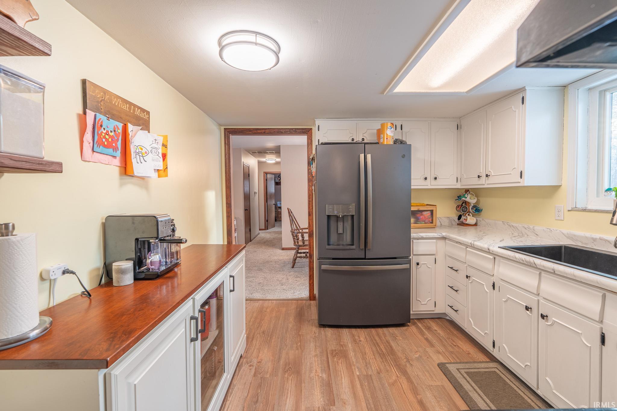 Kitchen featuring stainless steel fridge with ice dispenser, white cabinets, light wood-style floors, and extractor fan