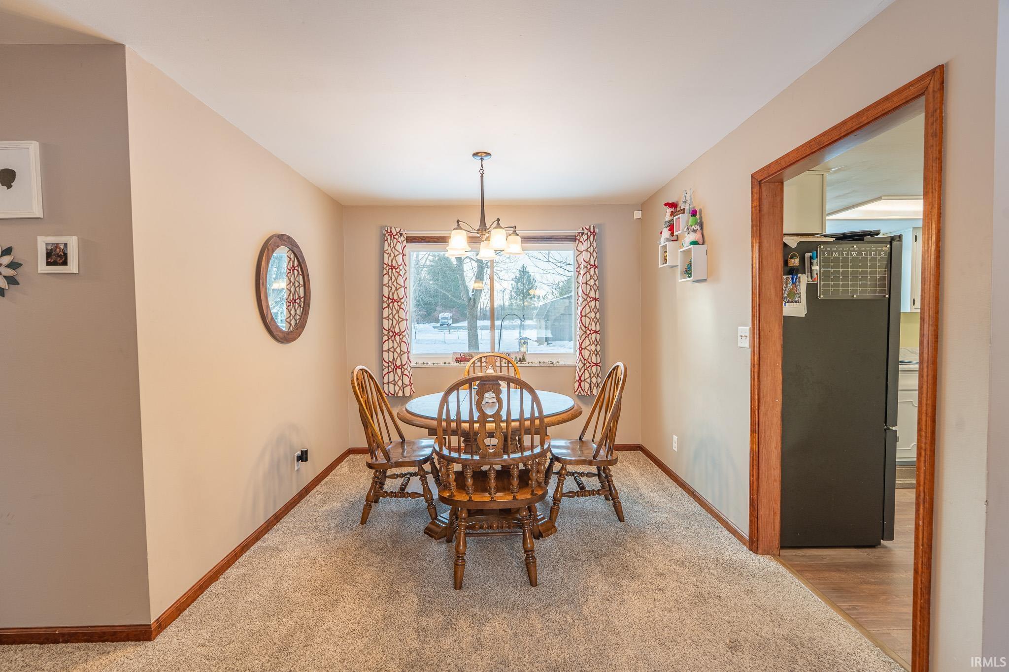 Carpeted dining space with a chandelier and baseboards