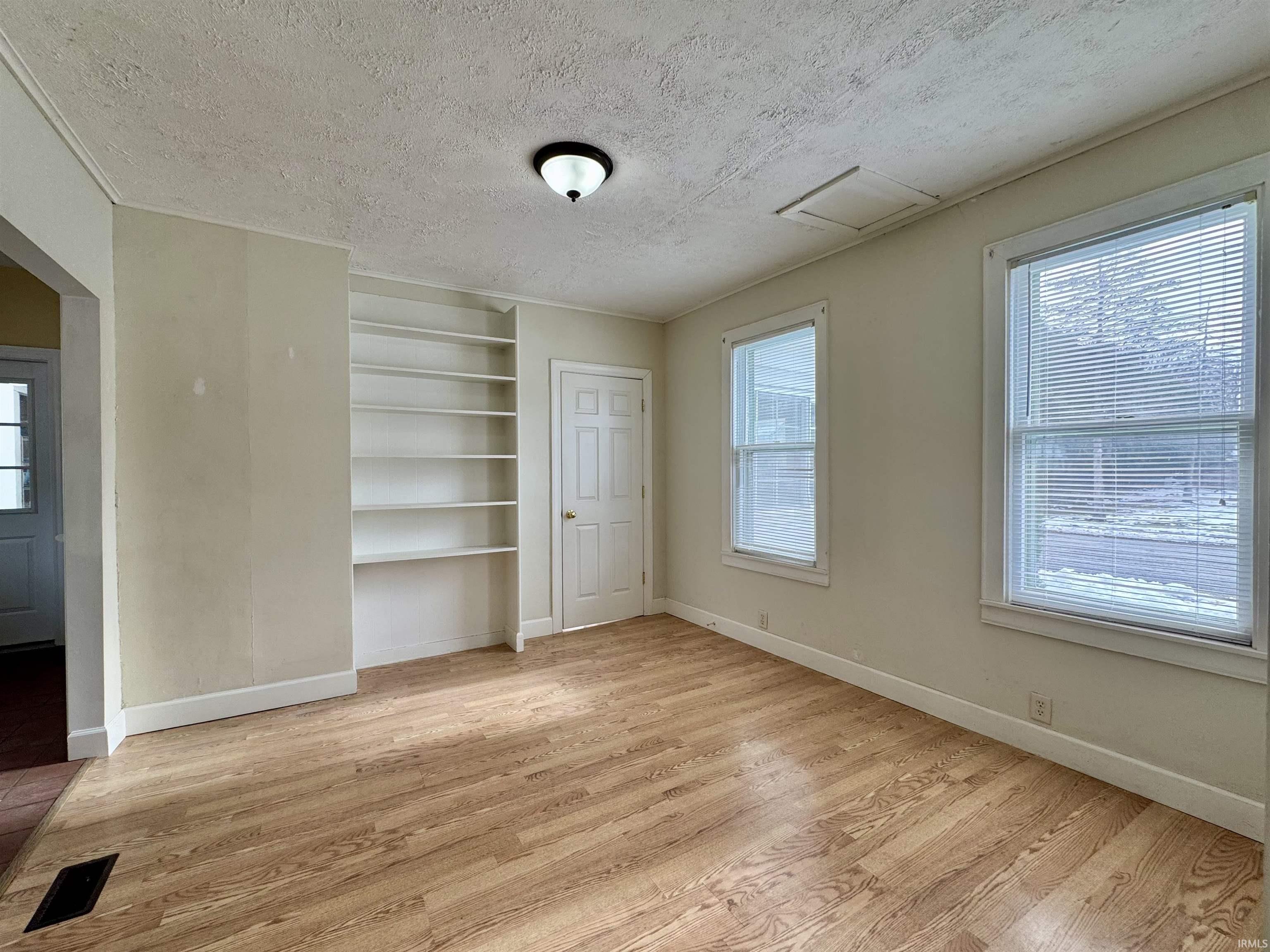 Unfurnished dining area with built in shelves, light wood finished floors, a textured ceiling, and attic access