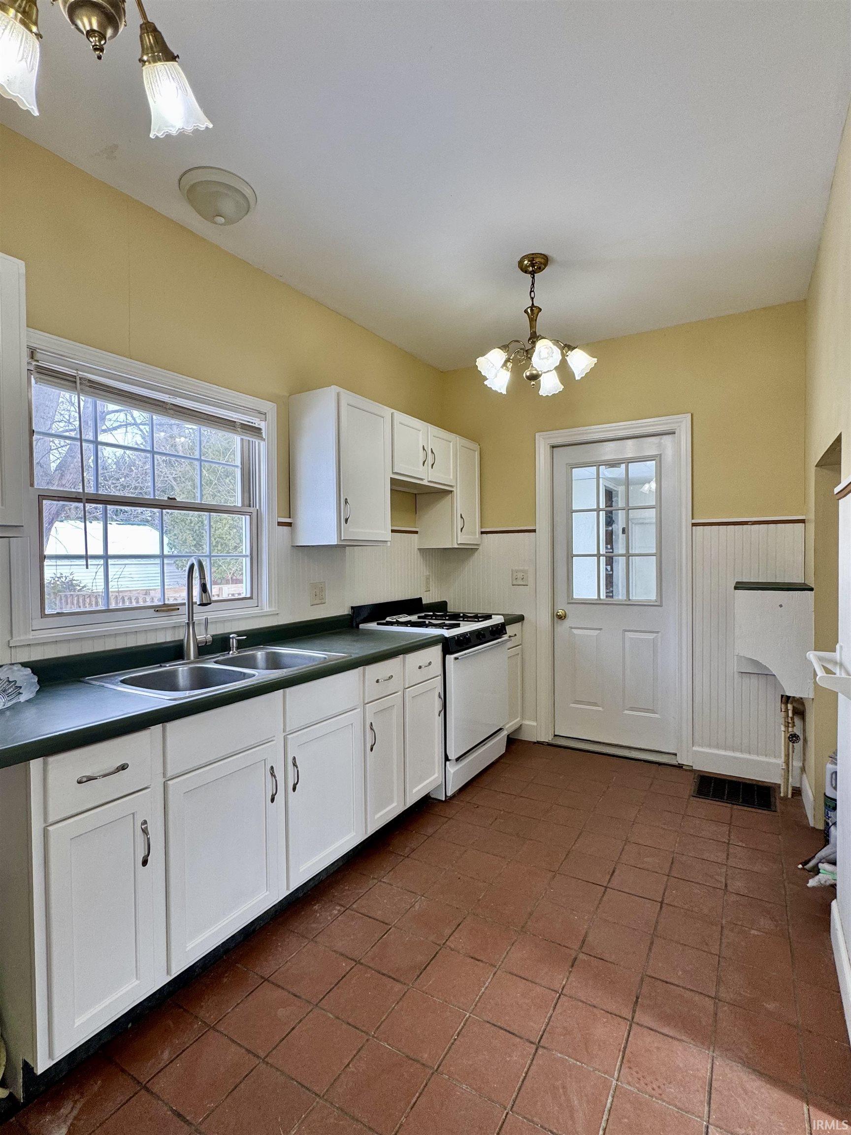 Kitchen with white cabinets, white range with gas cooktop, a chandelier, dark countertops, and hanging light fixtures