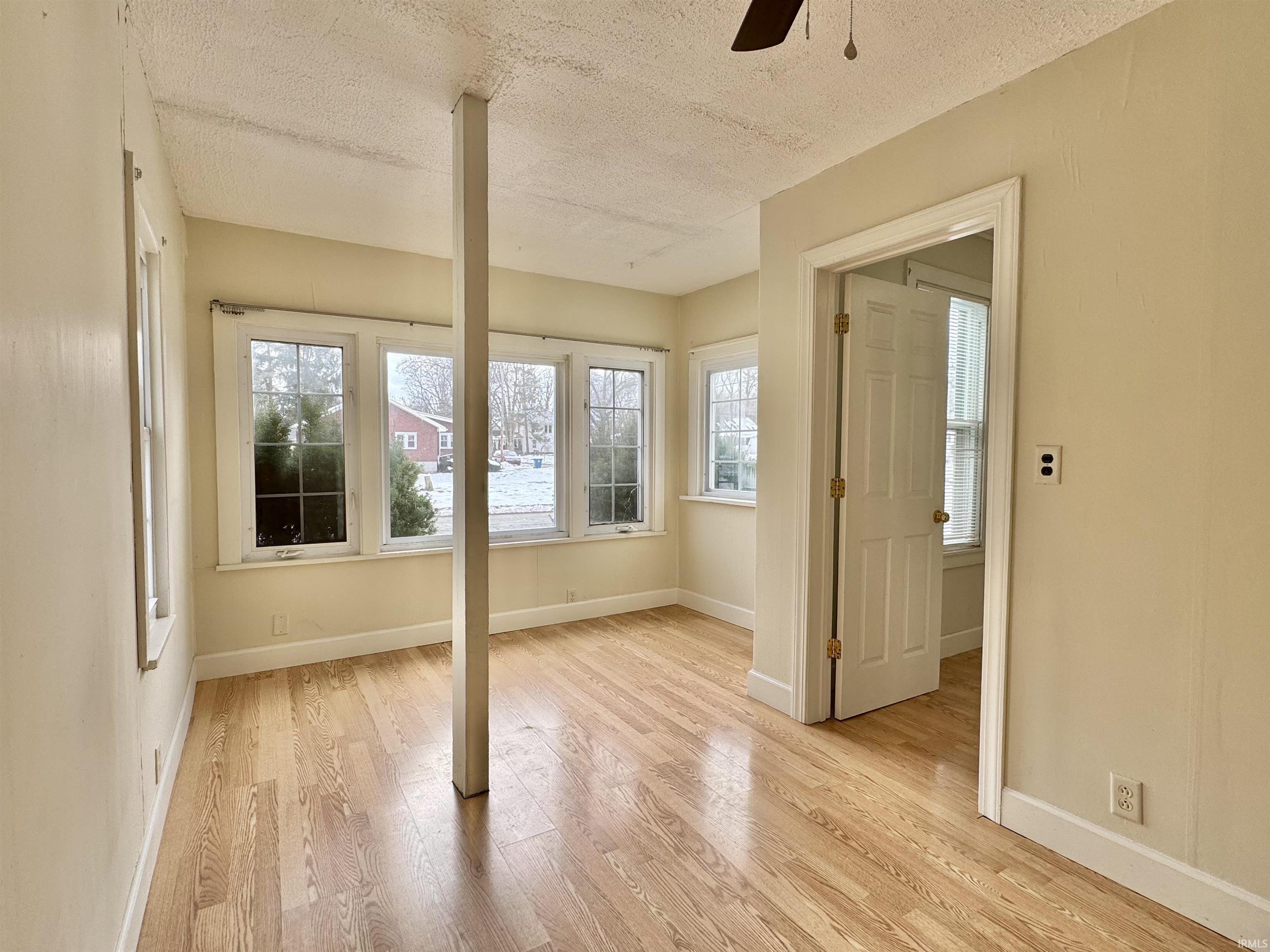 Empty room featuring light wood-style floors, a textured ceiling, and a ceiling fan