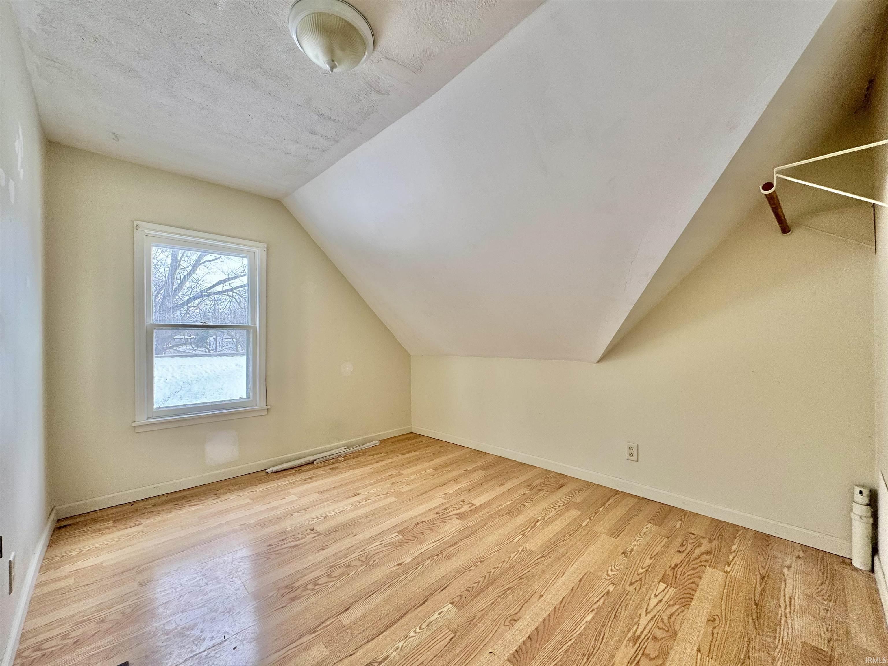 Additional living space featuring light wood-style flooring, lofted ceiling, and a textured ceiling