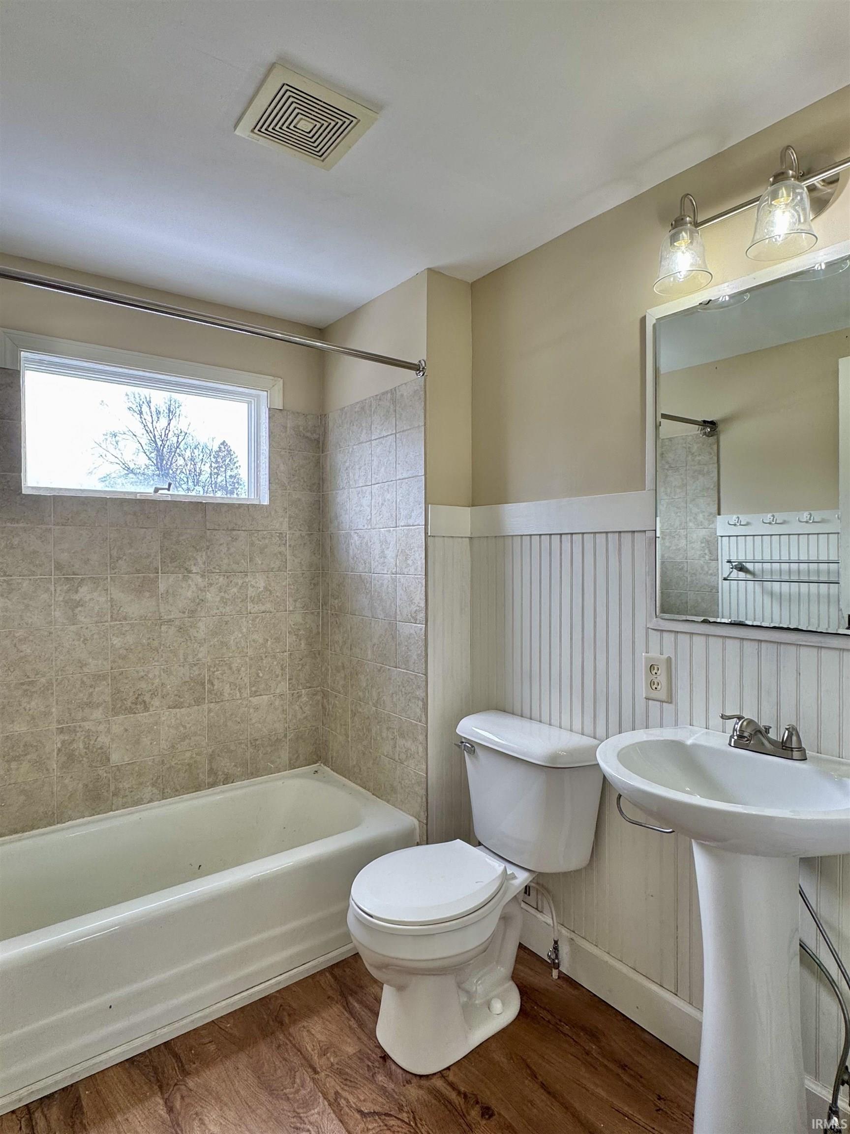 Bathroom featuring wood finished floors, bathing tub / shower combination, and a wainscoted wall