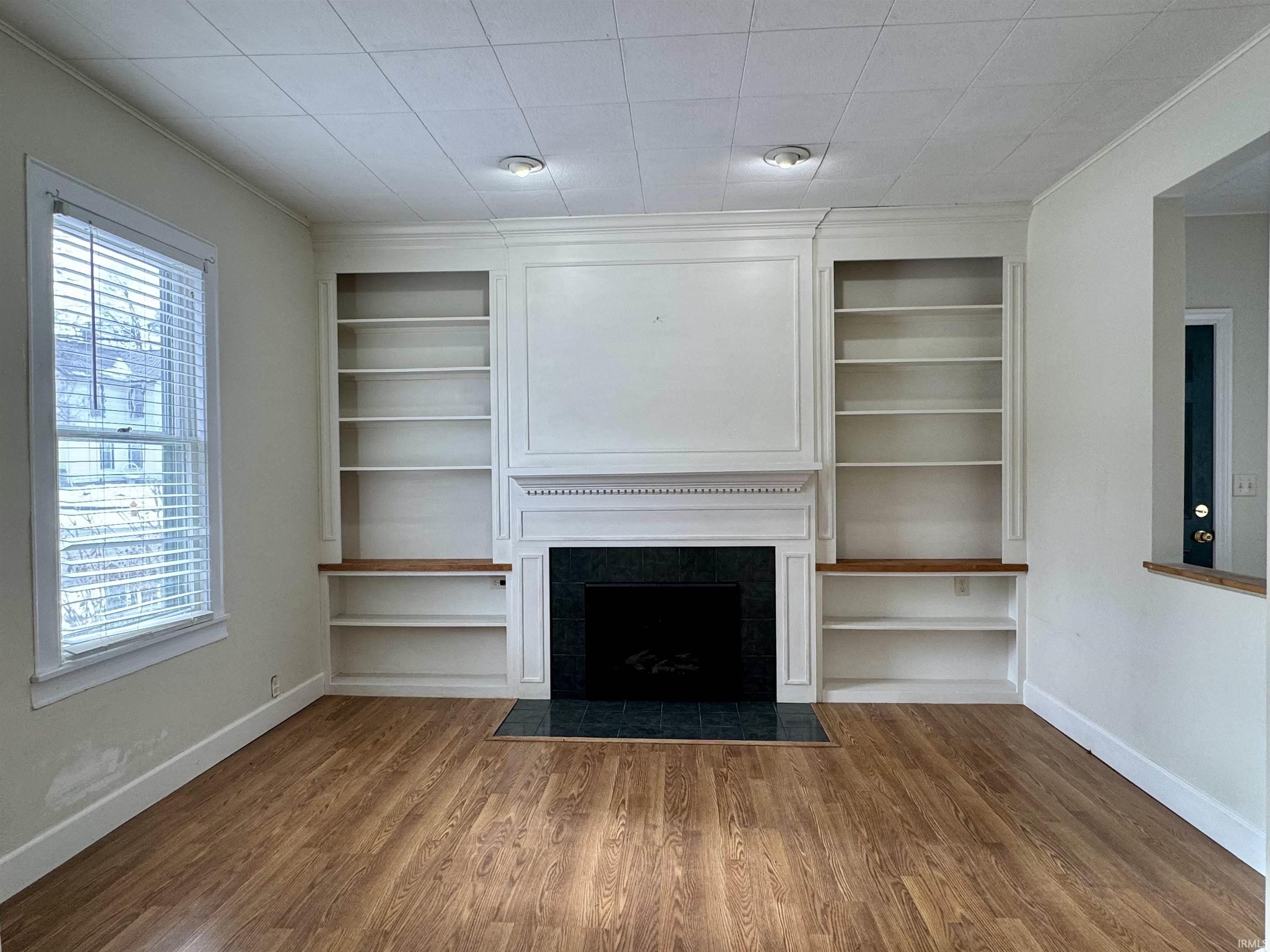 Unfurnished living room with wood finished floors, a tiled fireplace, and built in shelves