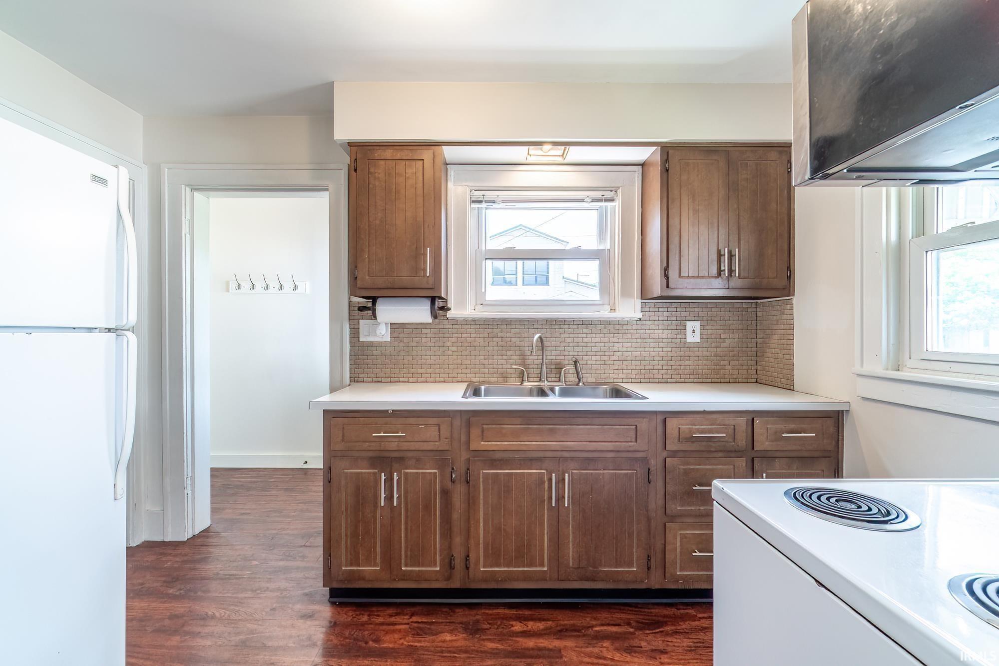 Kitchen with white appliances, light countertops, dark wood finished floors, tasteful backsplash, and extractor fan