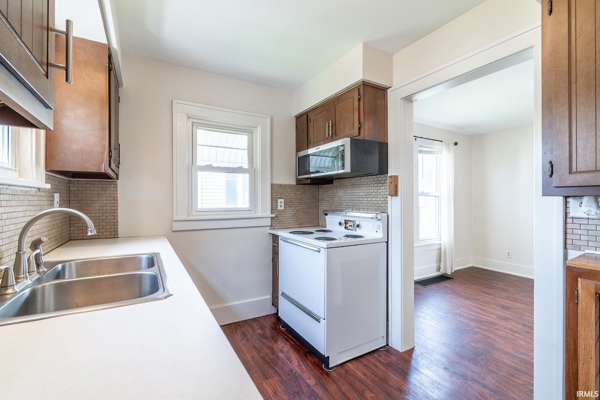Kitchen featuring white electric range, tasteful backsplash, light countertops, and dark wood finished floors