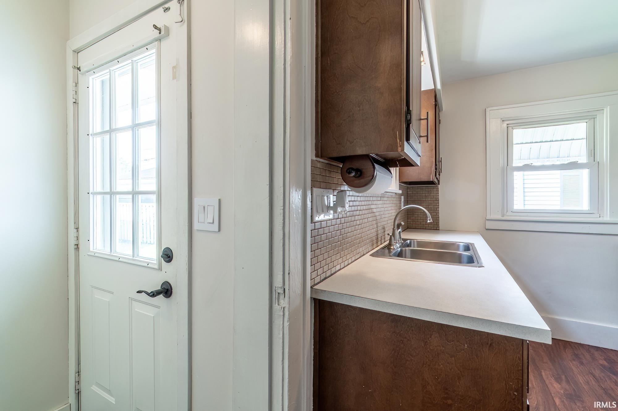 Kitchen with light countertops, dark brown cabinetry, decorative backsplash, and dark wood-style floors