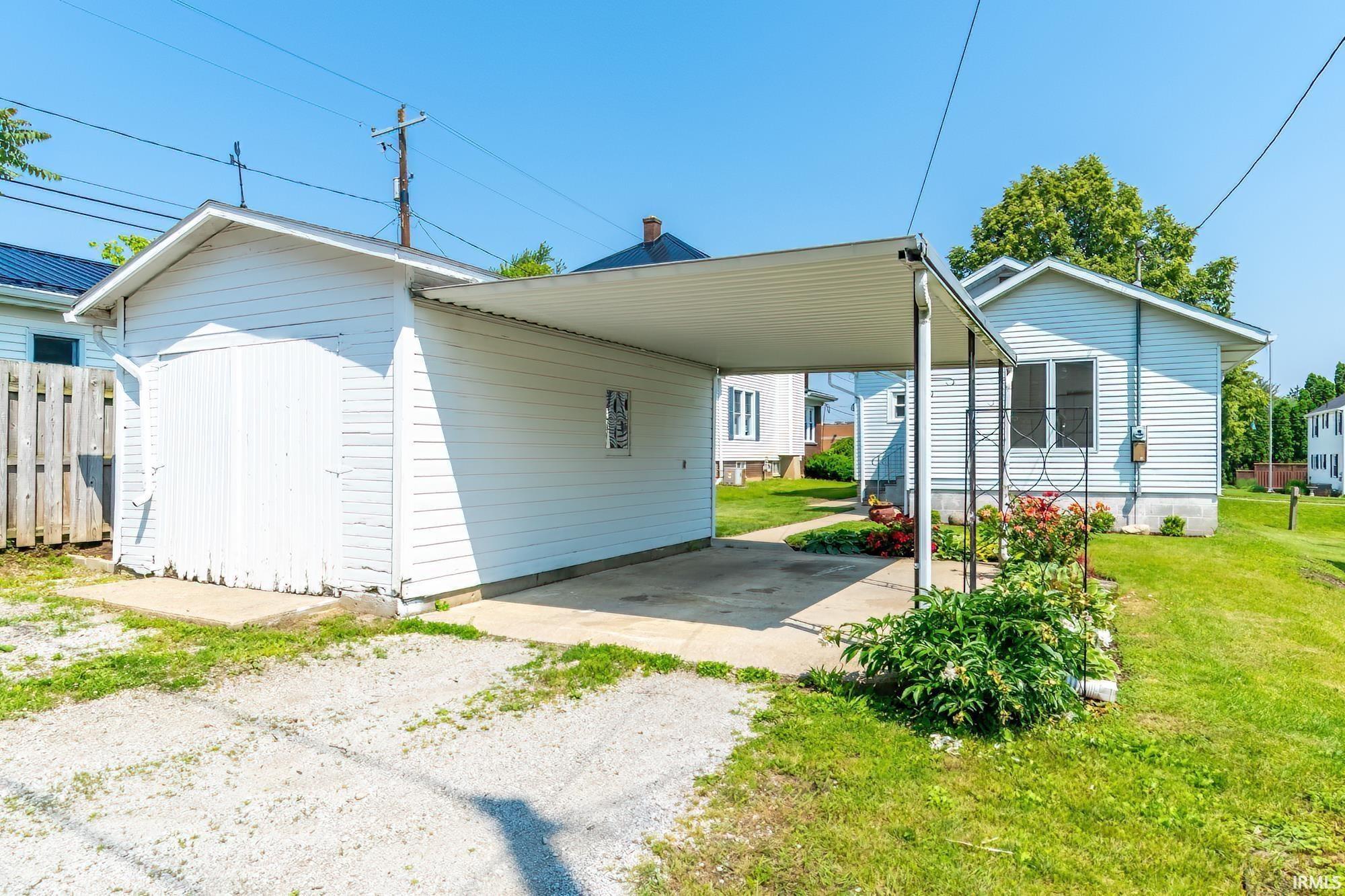 Back of house with a lawn, driveway, a carport, and an outbuilding