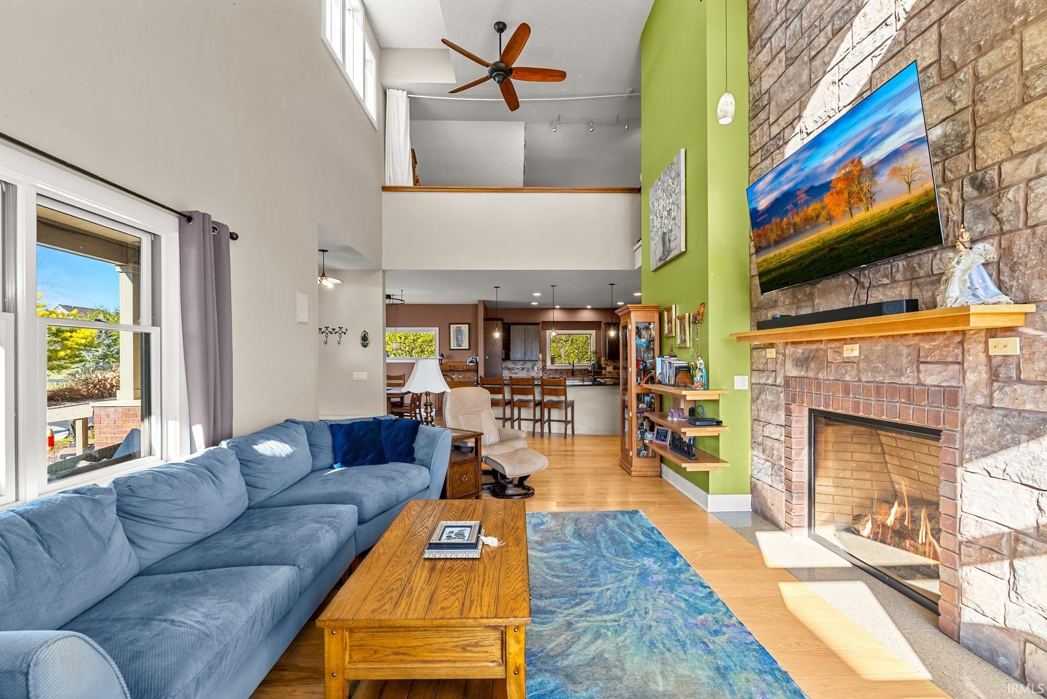 Living area featuring wood finished floors, a fireplace, a ceiling fan, and a towering ceiling