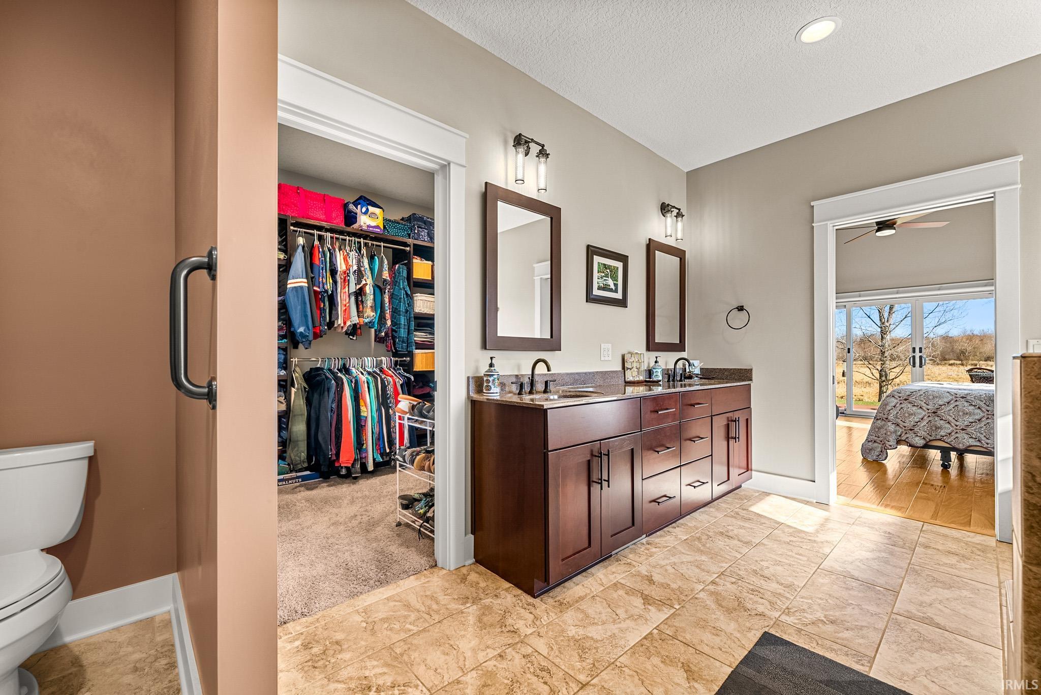 Bathroom featuring double vanity, connected bathroom, a spacious closet, ceiling fan, and a textured ceiling