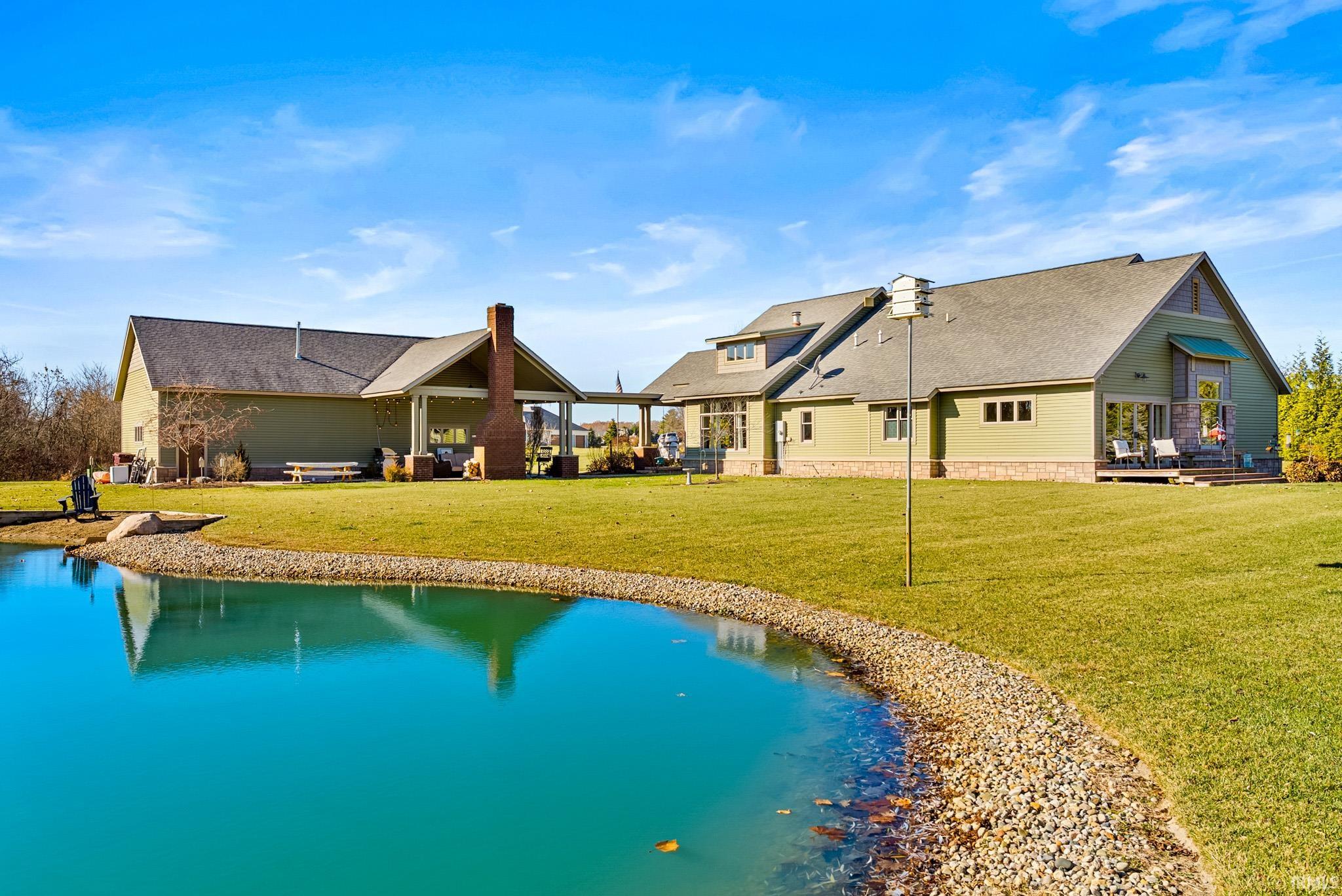 Rear view of property featuring a lawn, a patio area, roof with shingles, a chimney, and a water view