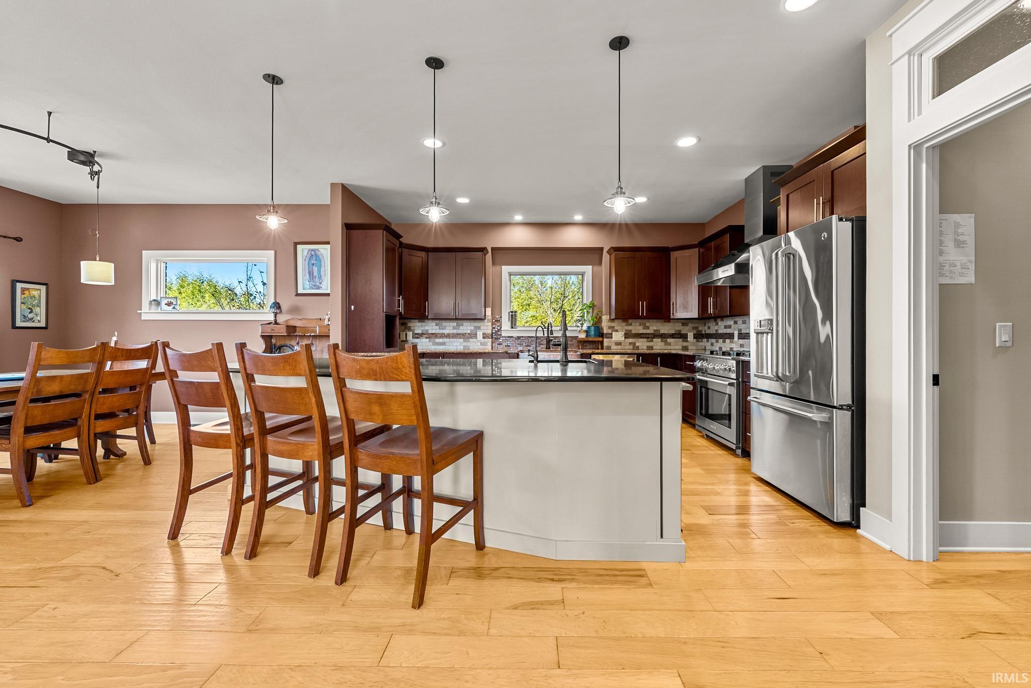 Kitchen featuring appliances with stainless steel finishes, backsplash, a kitchen bar, hanging light fixtures, and light wood-type flooring