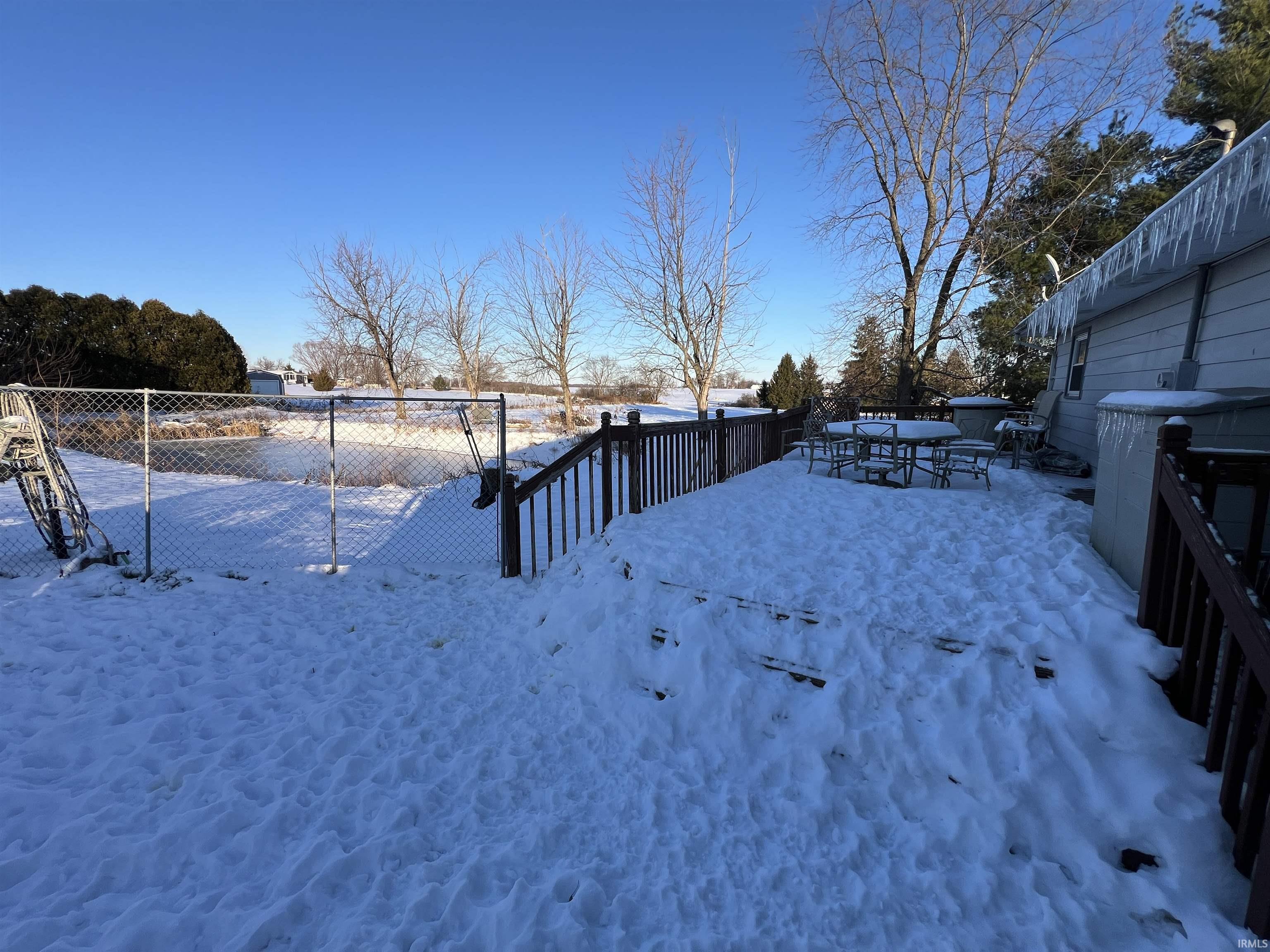 Yard covered in snow with a wooden deck and outdoor dining area