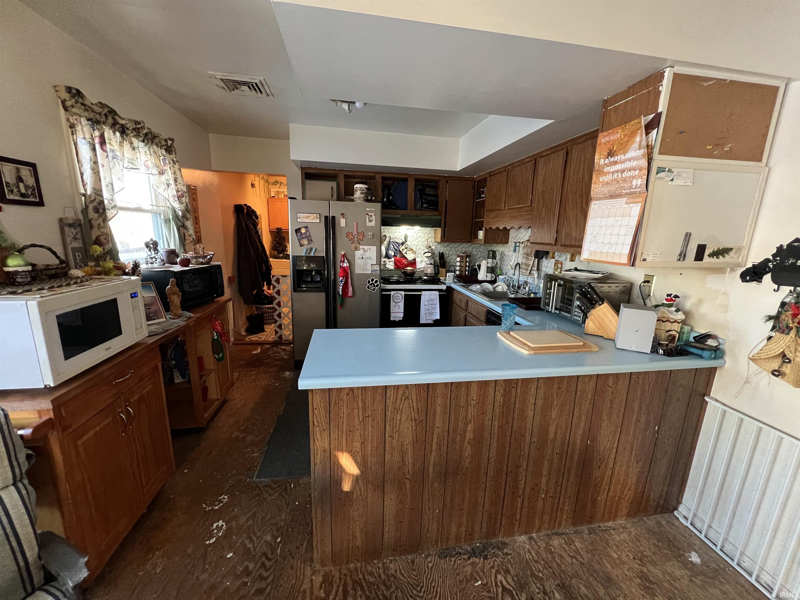 Kitchen with black appliances, a peninsula, light countertops, tasteful backsplash, and brown cabinetry