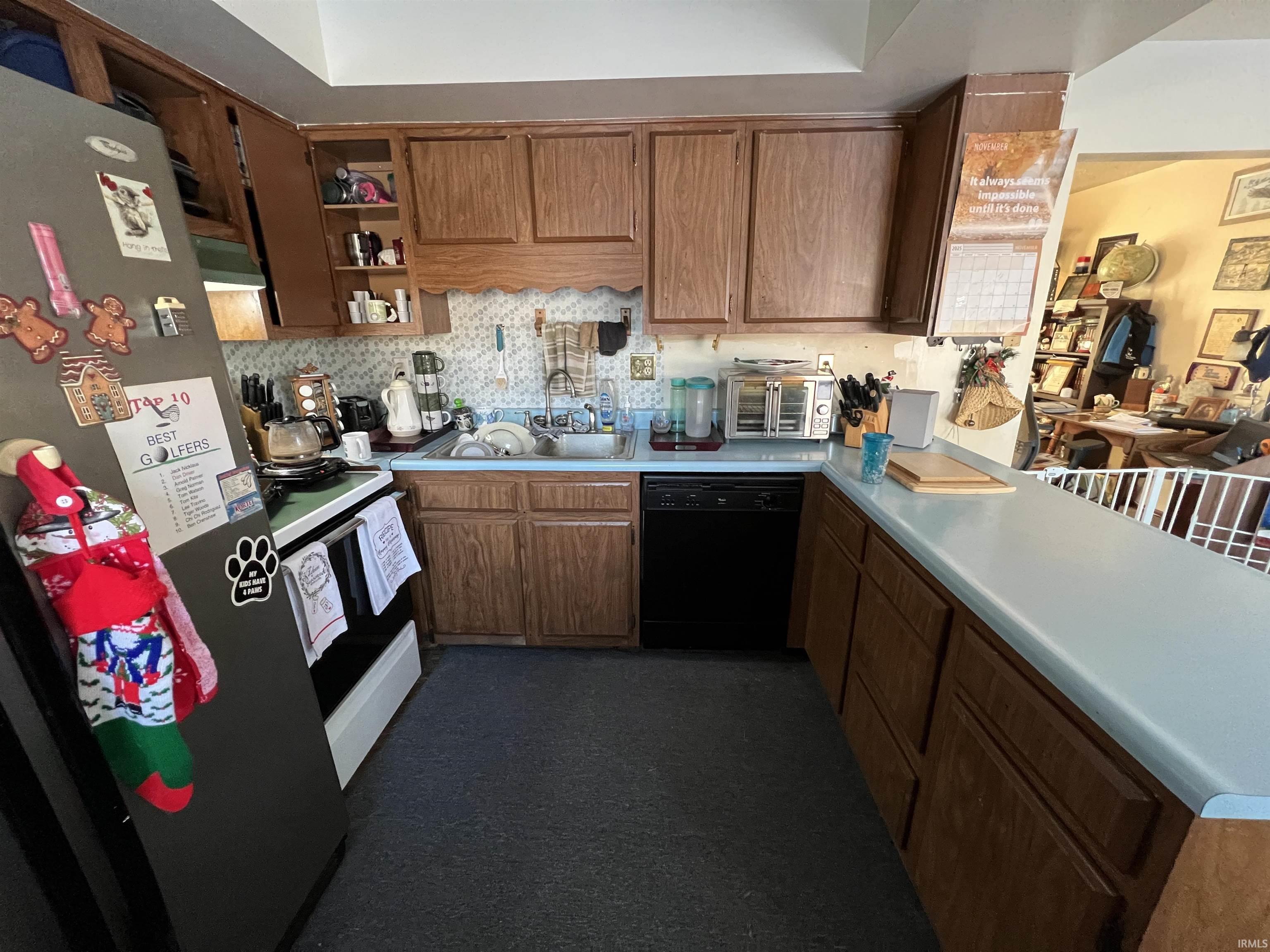 Kitchen with black appliances, a peninsula, light countertops, and brown cabinetry