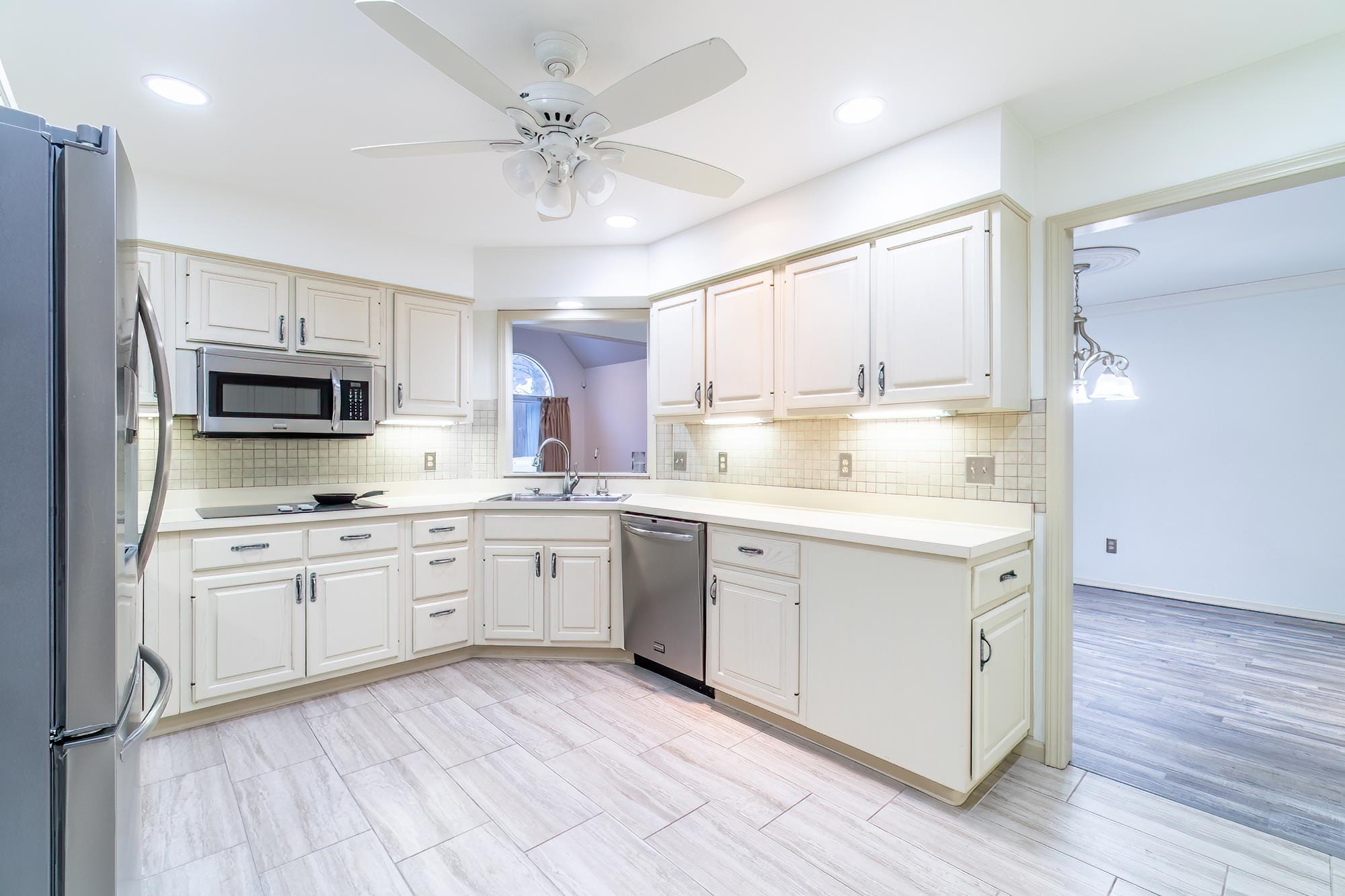 Kitchen with appliances with stainless steel finishes, light countertops, a ceiling fan, and decorative backsplash