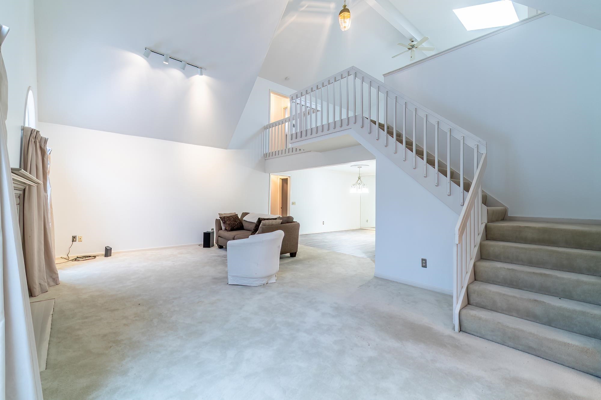 Unfurnished living room featuring high vaulted ceiling, a ceiling fan, track lighting, stairs, and a chandelier