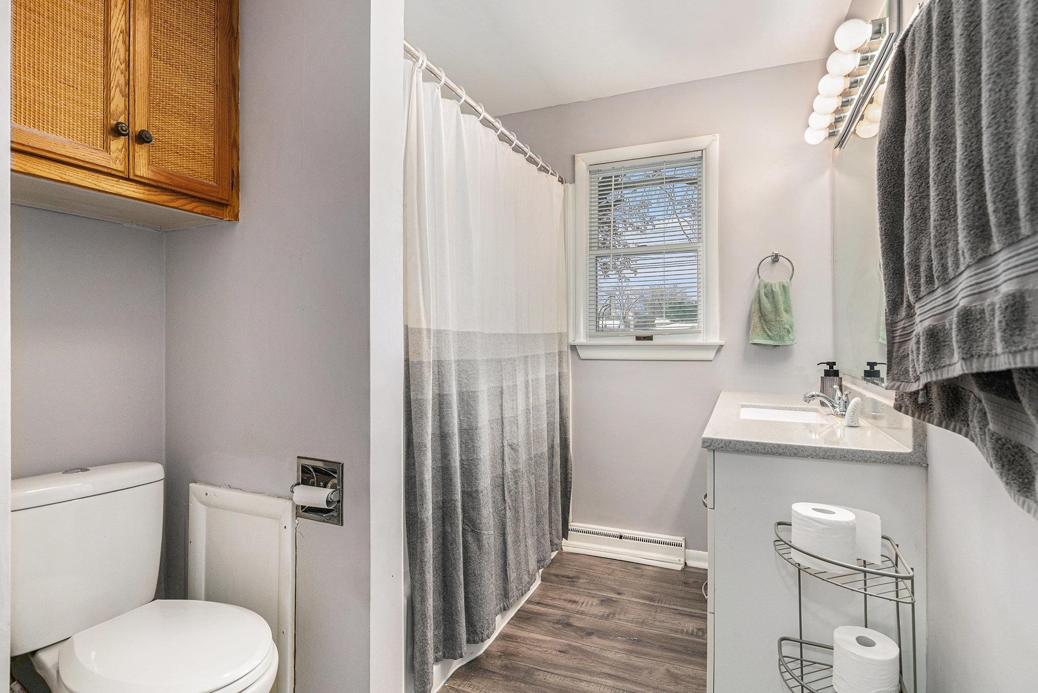 Full bath featuring vanity, curtained shower, a baseboard radiator, and dark wood-style floors