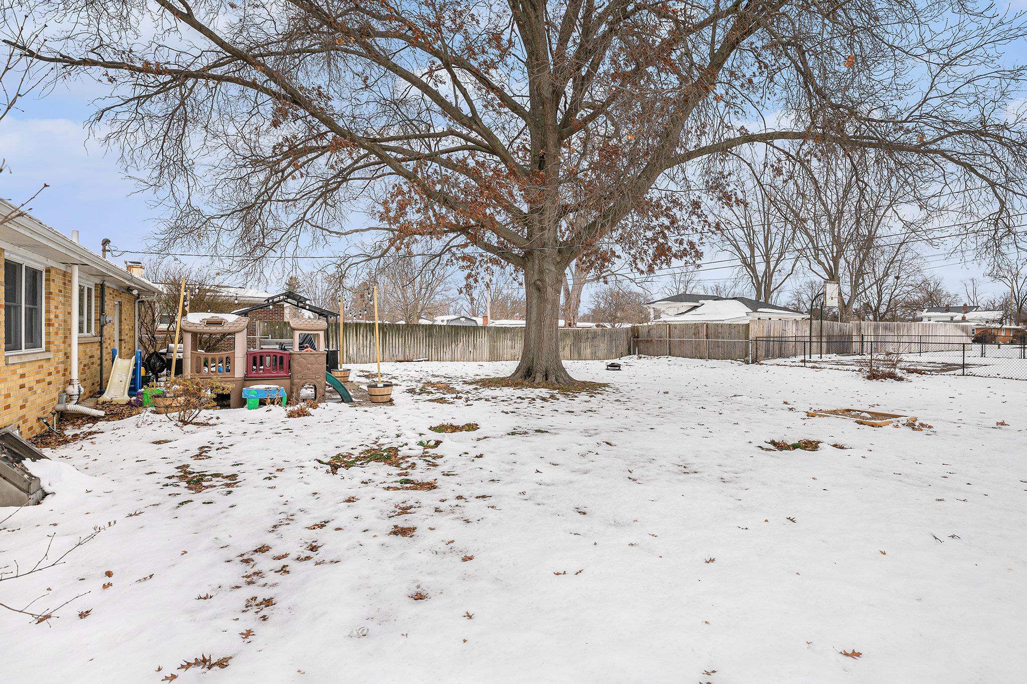 Snowy yard with a fenced backyard and a playground