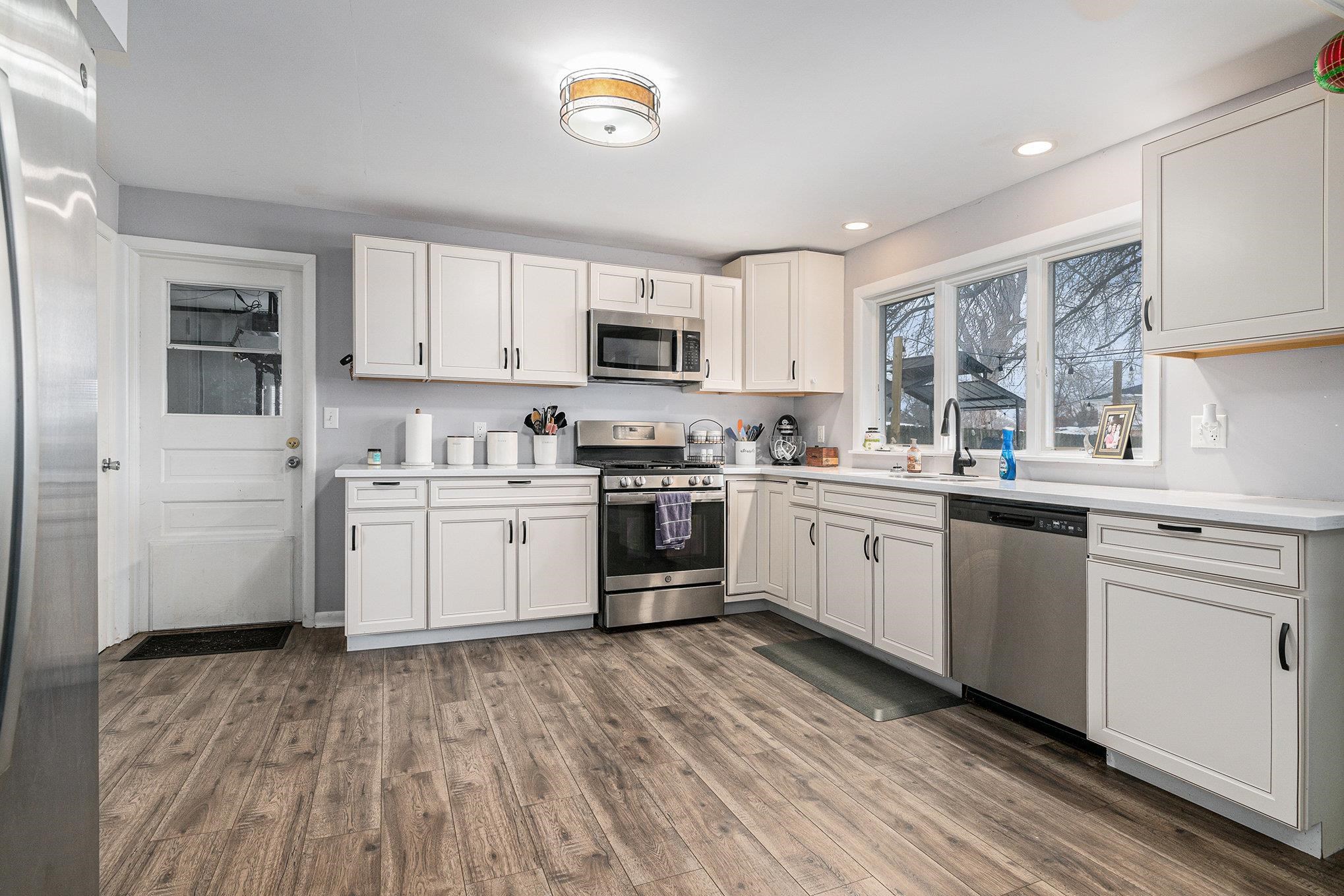 Kitchen with appliances with stainless steel finishes, light countertops, dark wood-type flooring, white cabinetry, and recessed lighting