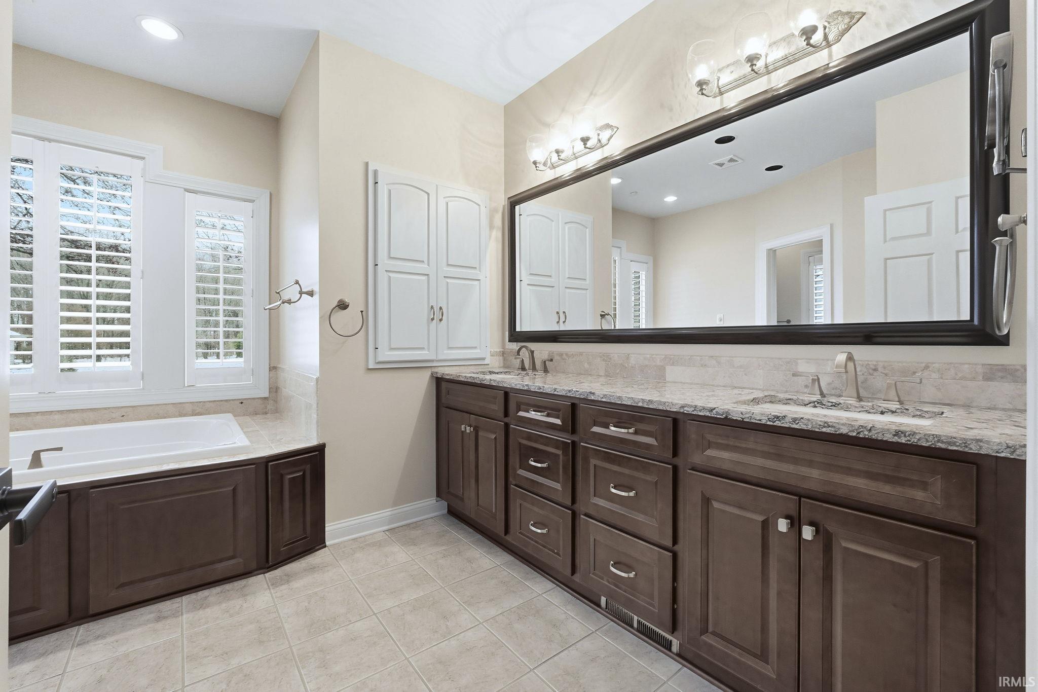 Double vanity, cherry cabinetry, granite countertops, a garden tub, tiled floor, and recessed lighting