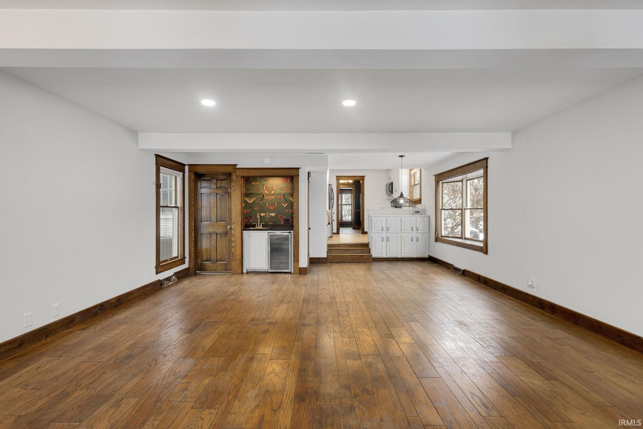 Unfurnished living room with beverage cooler, dark wood-type flooring, and recessed lighting