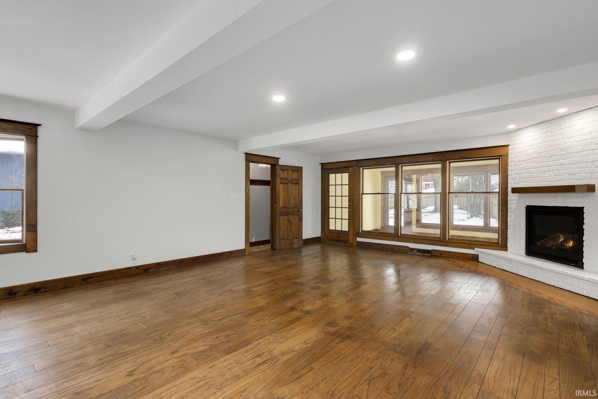 Unfurnished living room featuring healthy amount of natural light, a brick fireplace, wood-type flooring, beam ceiling, and recessed lighting