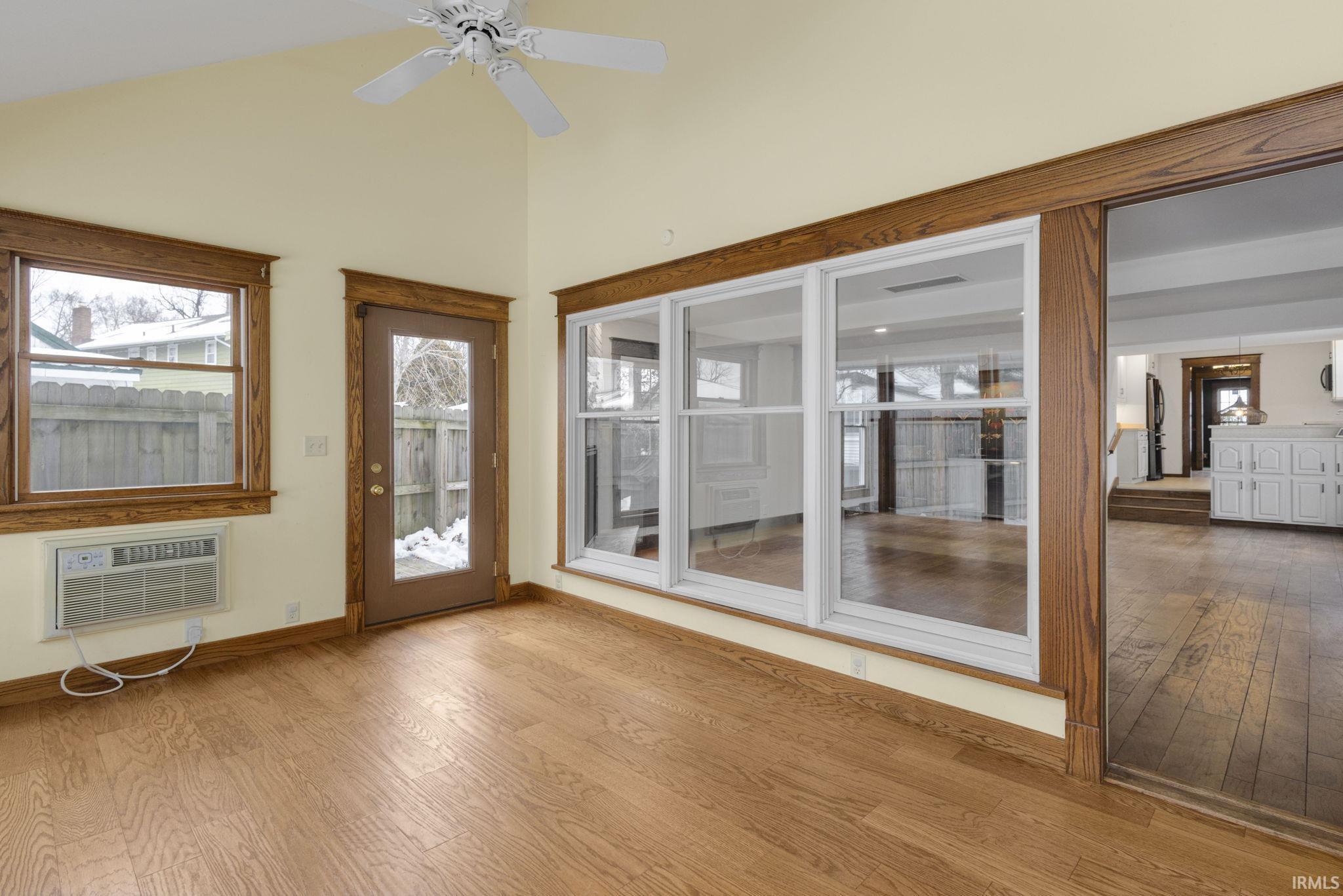 Unfurnished sunroom with hardwood / wood-style flooring, a wall mounted AC, and high vaulted ceiling