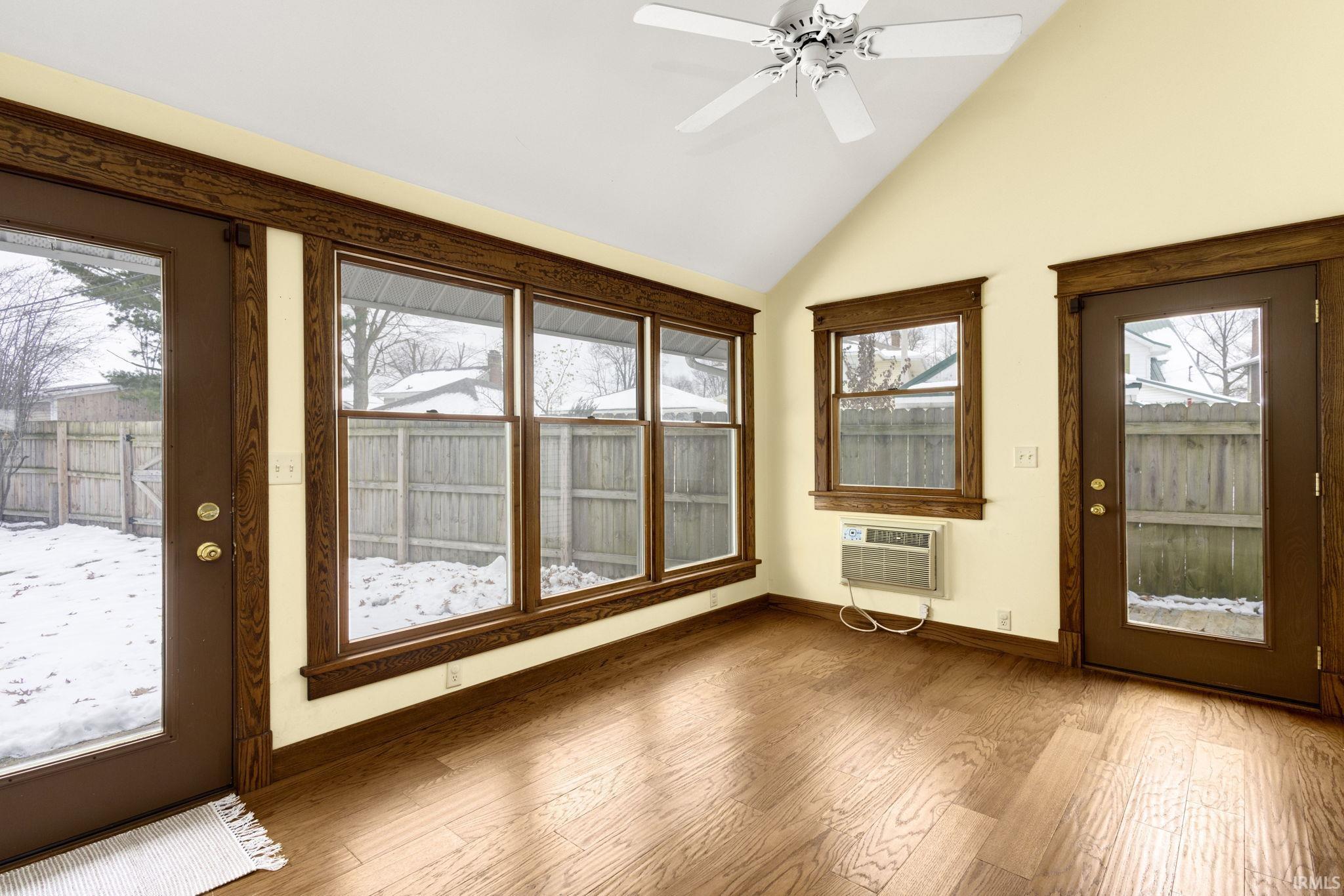 Unfurnished sunroom featuring healthy amount of natural light, wood-type flooring, and high vaulted ceiling