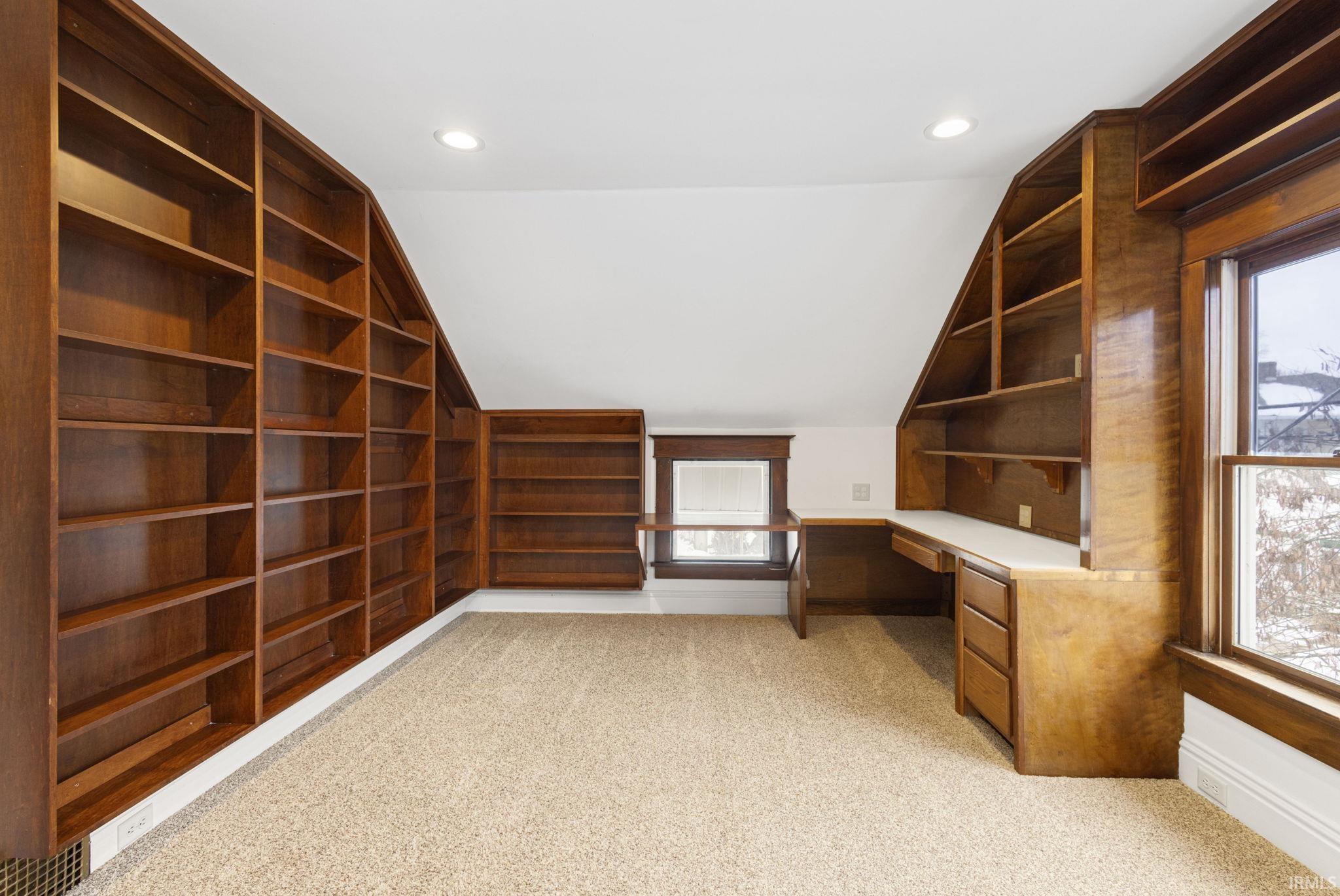 Unfurnished office with built in desk, light carpet, vaulted ceiling, recessed lighting, and built in shelves