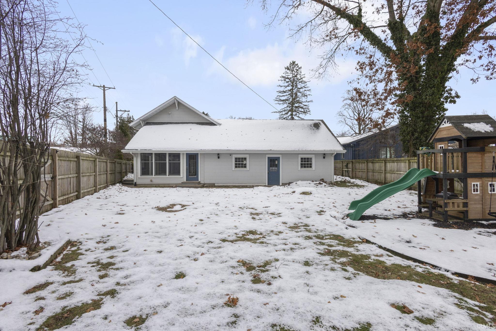 Snow covered back of property featuring a playground and a fenced backyard