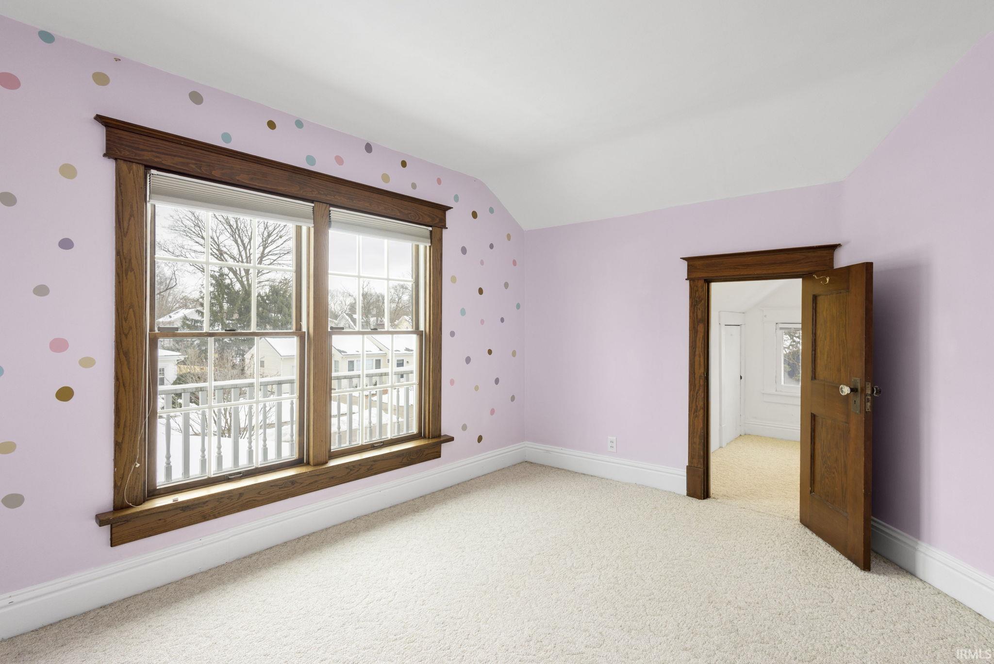 Carpeted empty room featuring vaulted ceiling and wallpapered walls