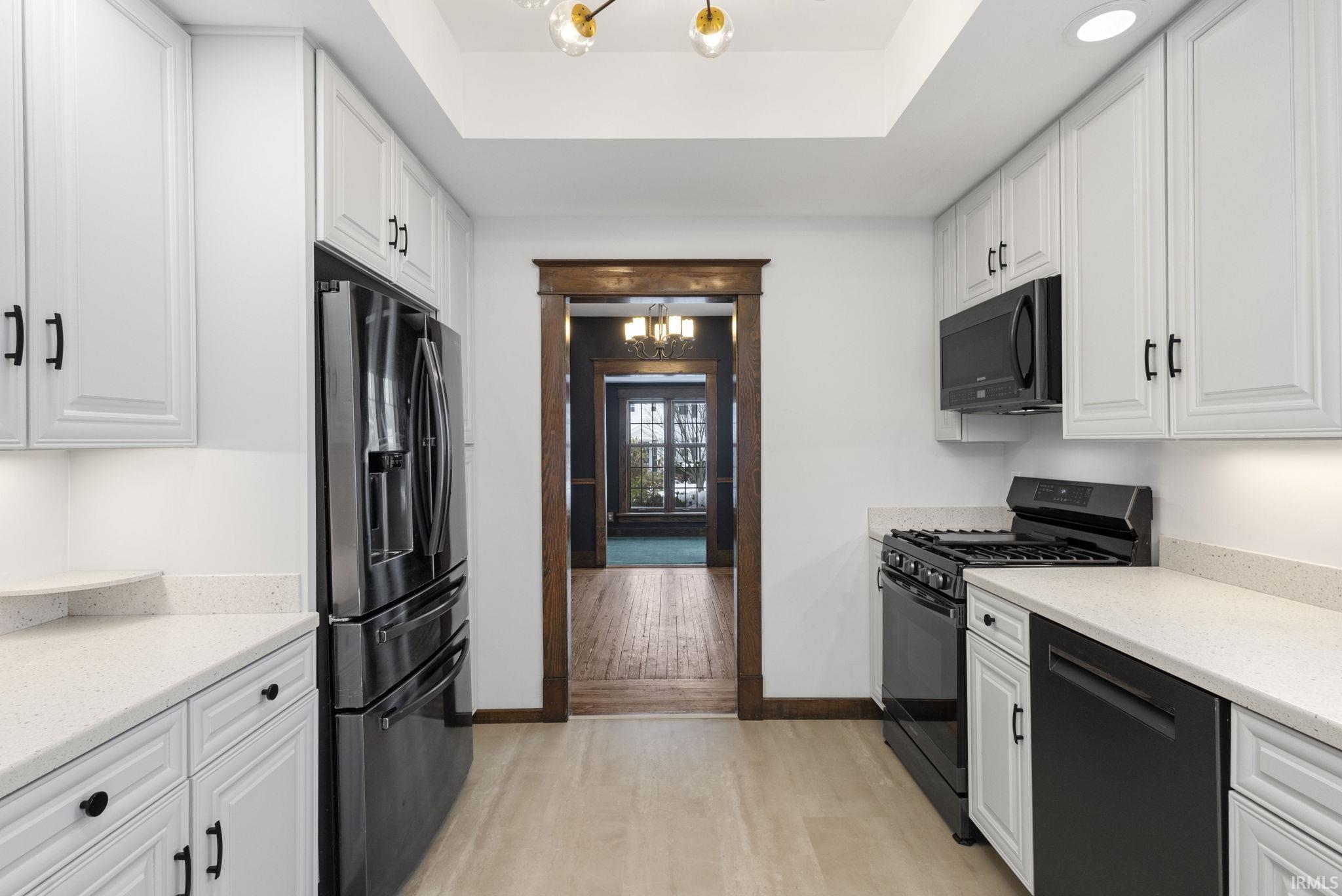 Kitchen featuring a chandelier, black appliances, white cabinetry, and light stone countertops