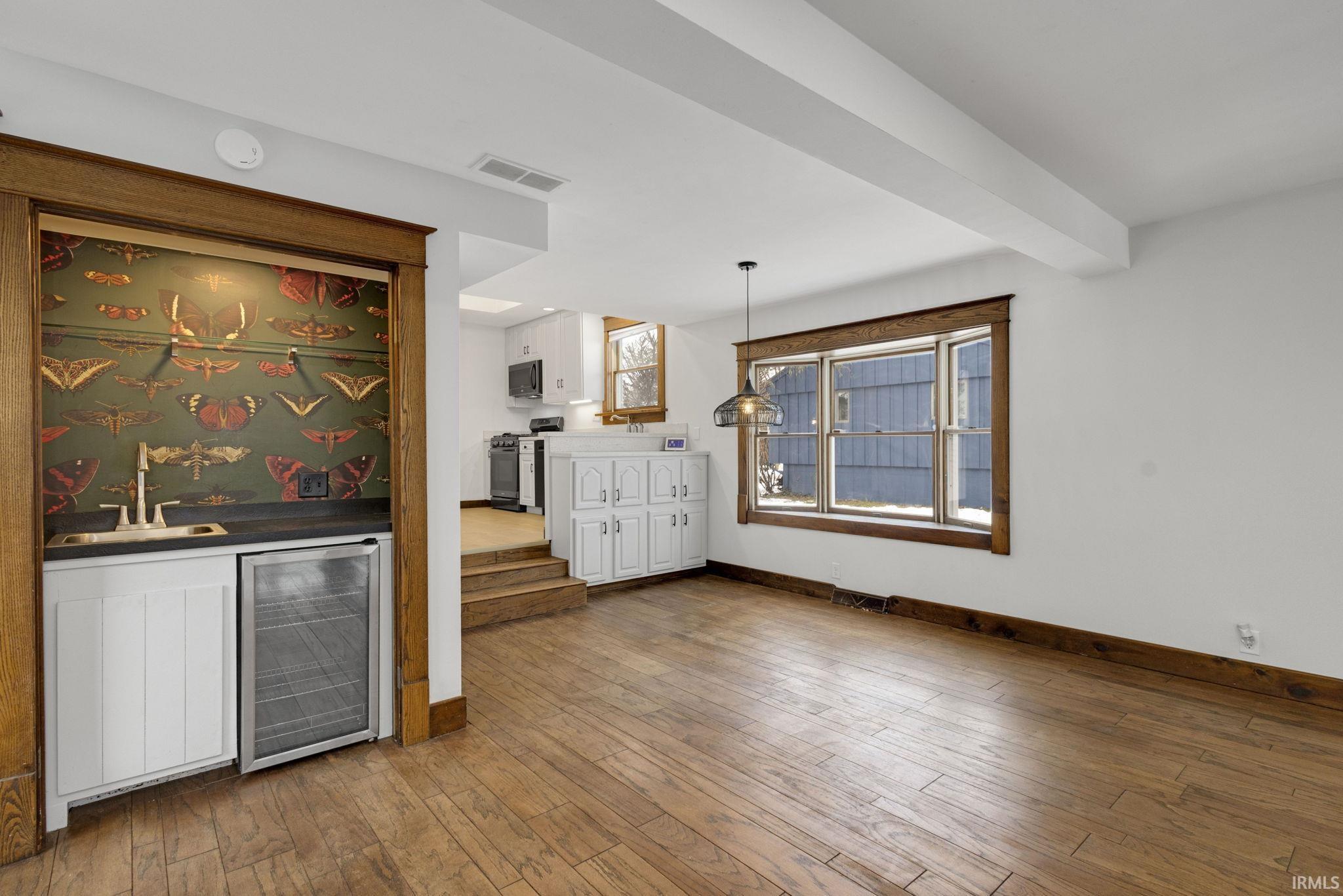 Indoor wet bar with white cabinetry, beverage cooler, light wood-type flooring, pendant lighting, and range with gas stovetop