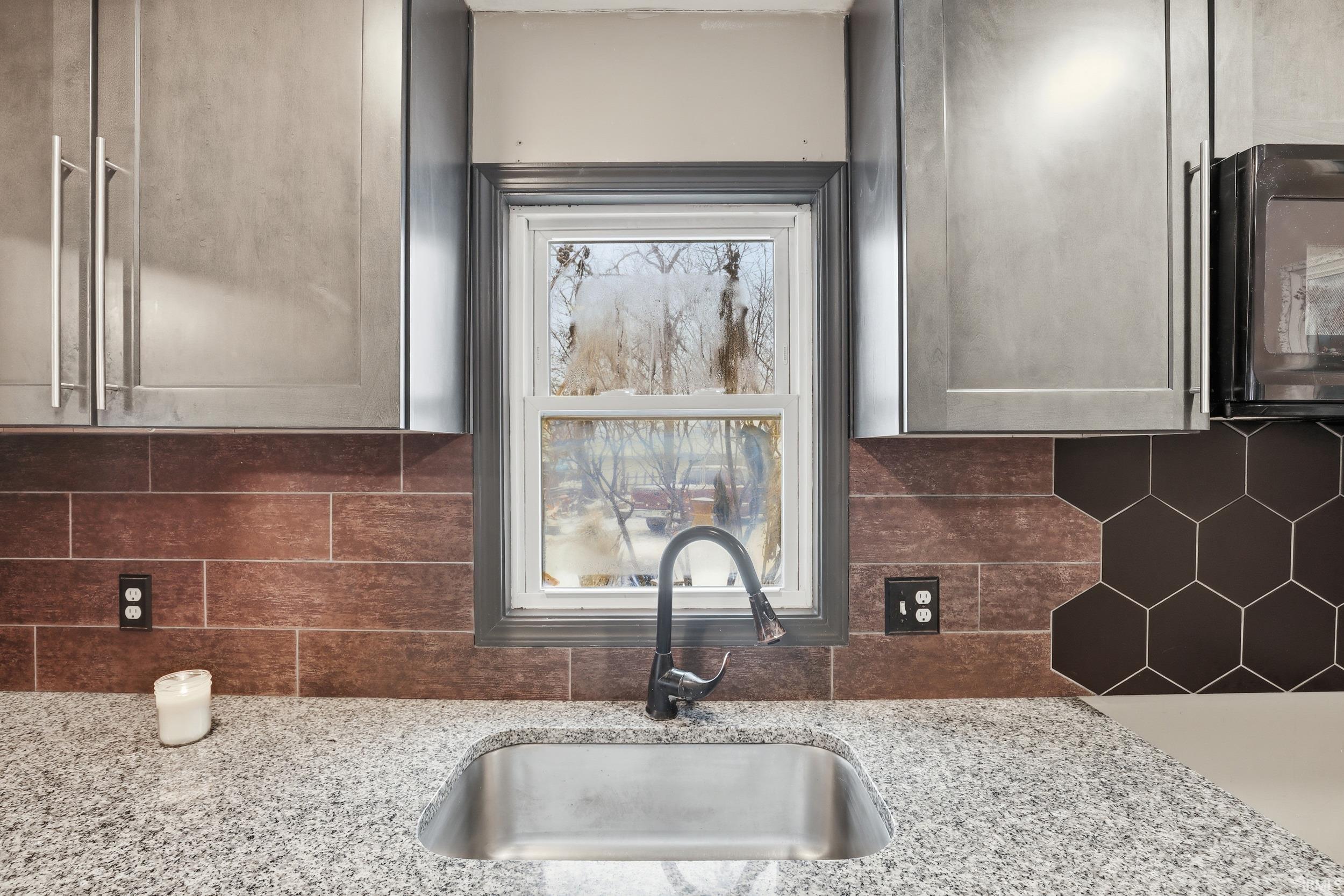 Kitchen with light stone counters, black microwave, and decorative backsplash