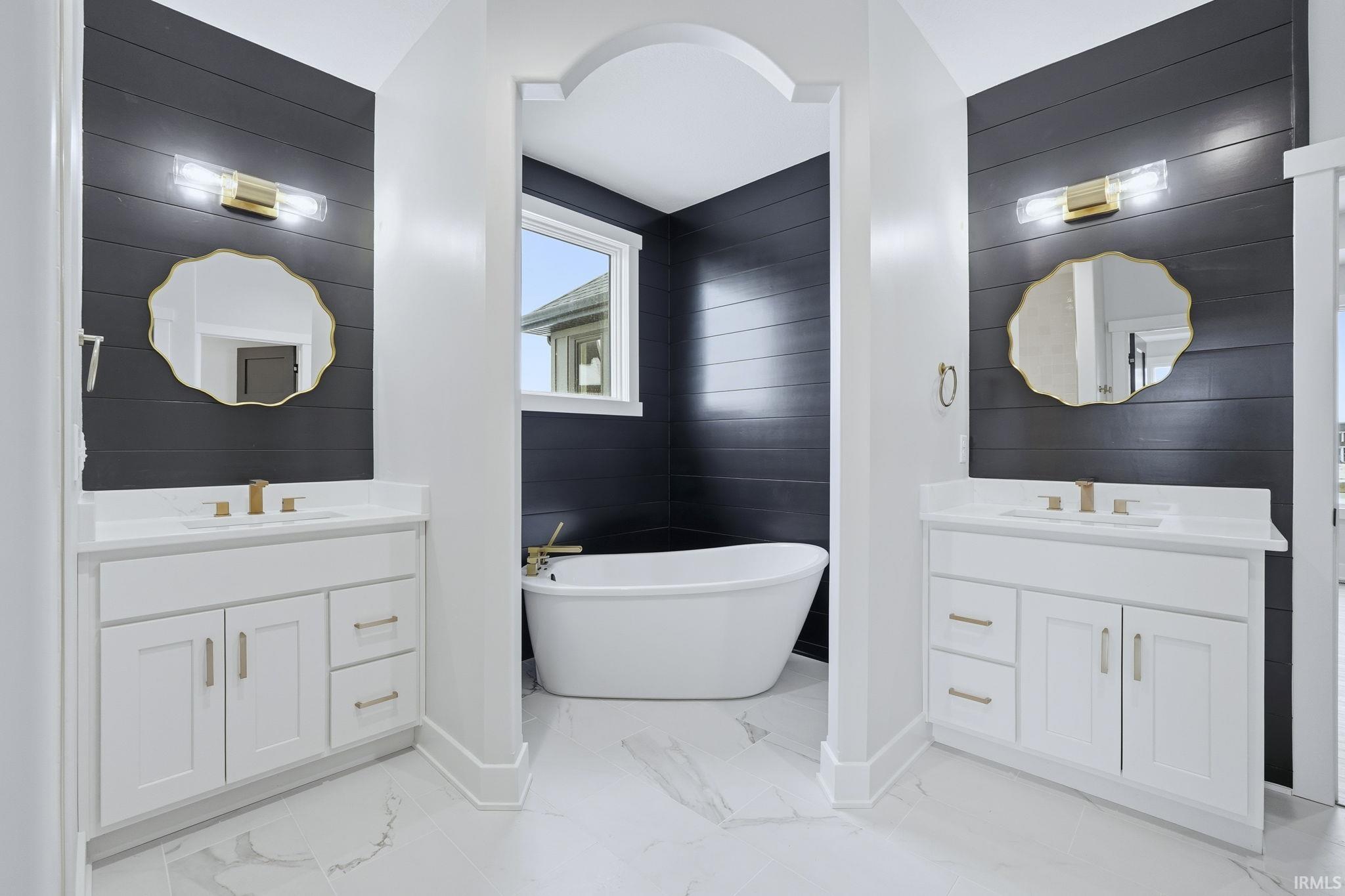 Bathroom with two vanities, light marble finish floors, a soaking tub, and wood walls