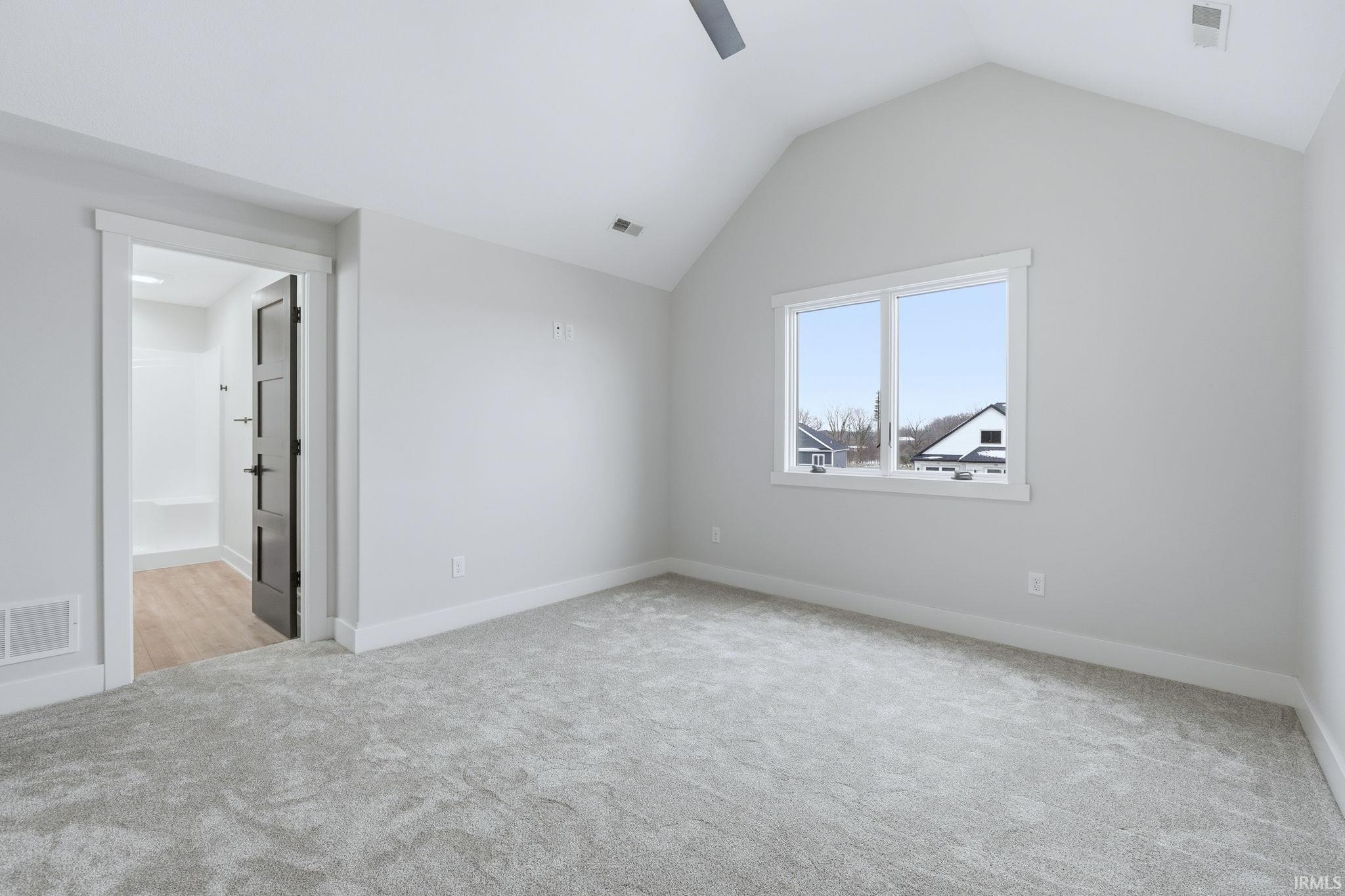 Unfurnished bedroom with light colored carpet, ceiling fan, vaulted ceiling, and ensuite bathroom