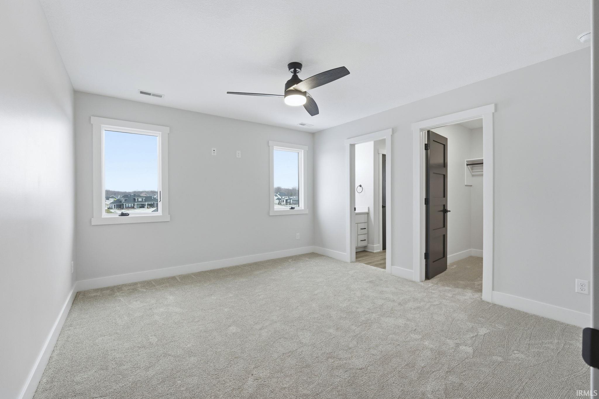 Unfurnished bedroom featuring a spacious closet, ceiling fan, light carpet, and ensuite bath