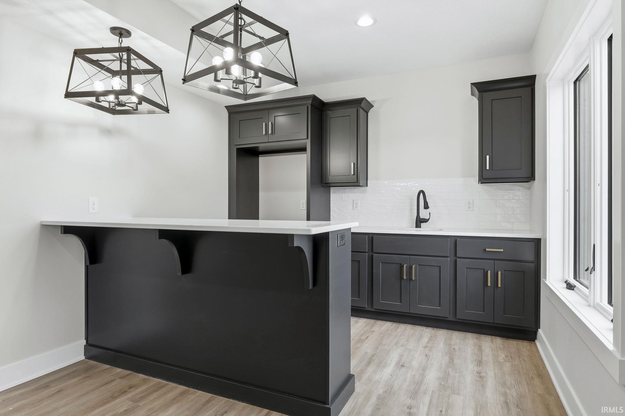 Kitchen featuring a kitchen bar, decorative backsplash, light wood-style flooring, a peninsula, and recessed lighting