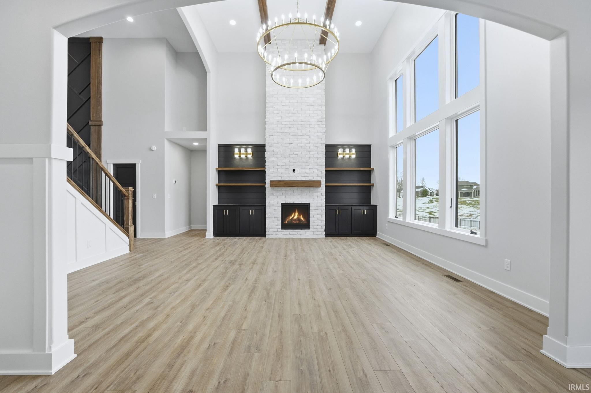 Unfurnished living room with light wood-style flooring, a towering ceiling, a stone fireplace, a chandelier, and stairway