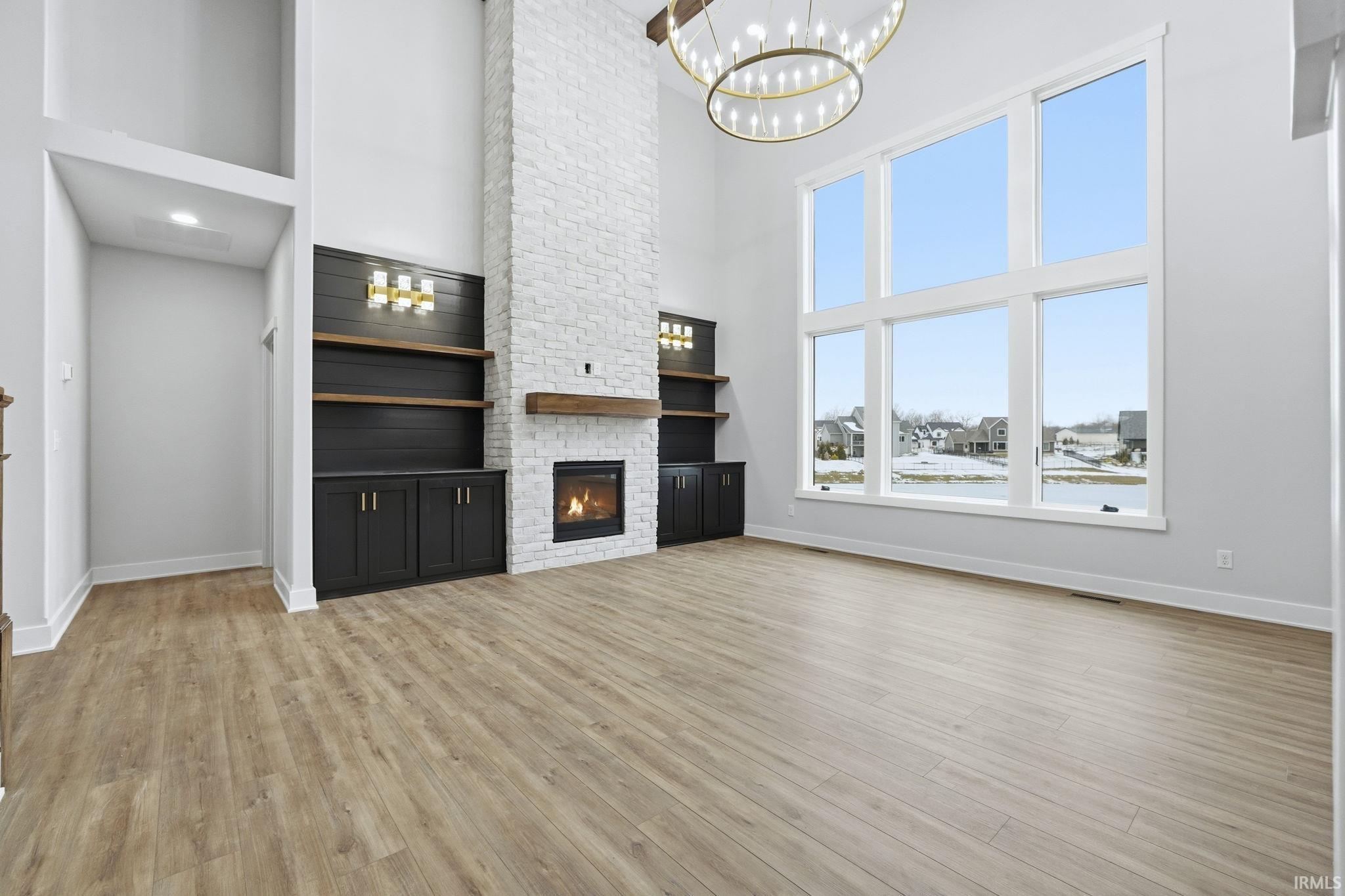 Unfurnished living room featuring a fireplace, light wood-style floors, a chandelier, and a towering ceiling