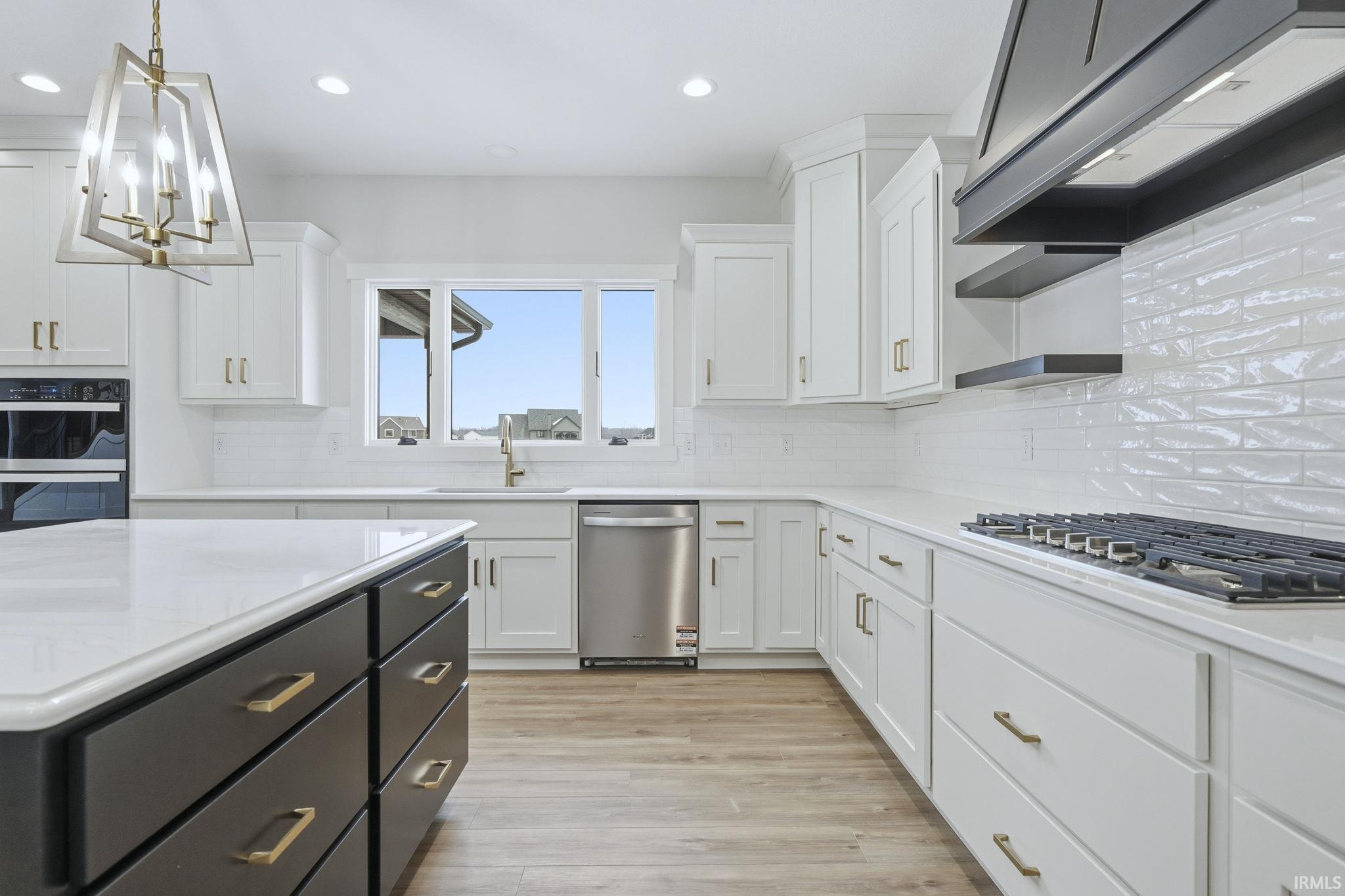 Kitchen with white cabinets, stainless steel appliances, range hood, pendant lighting, and light wood-type flooring
