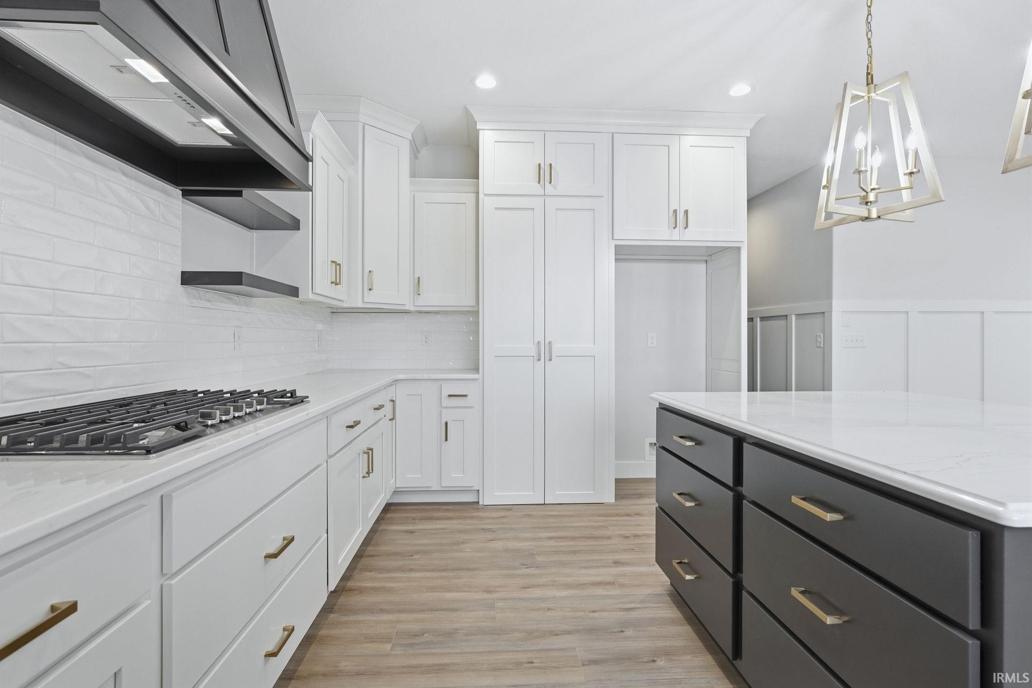 Kitchen with white cabinetry, custom exhaust hood, decorative backsplash, light wood finished floors, and stainless steel gas cooktop