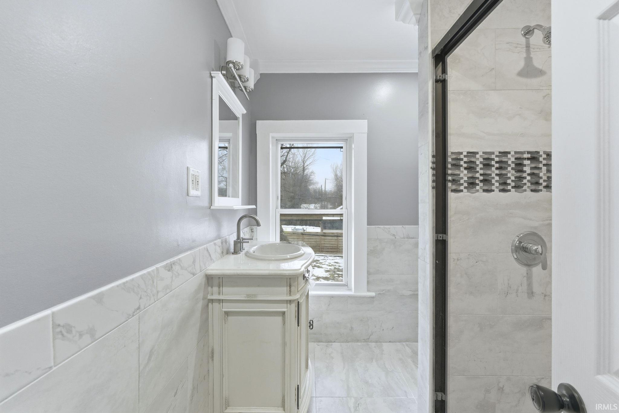 Full bath with tile walls, wainscoting, ornamental molding, a stall shower, and vanity