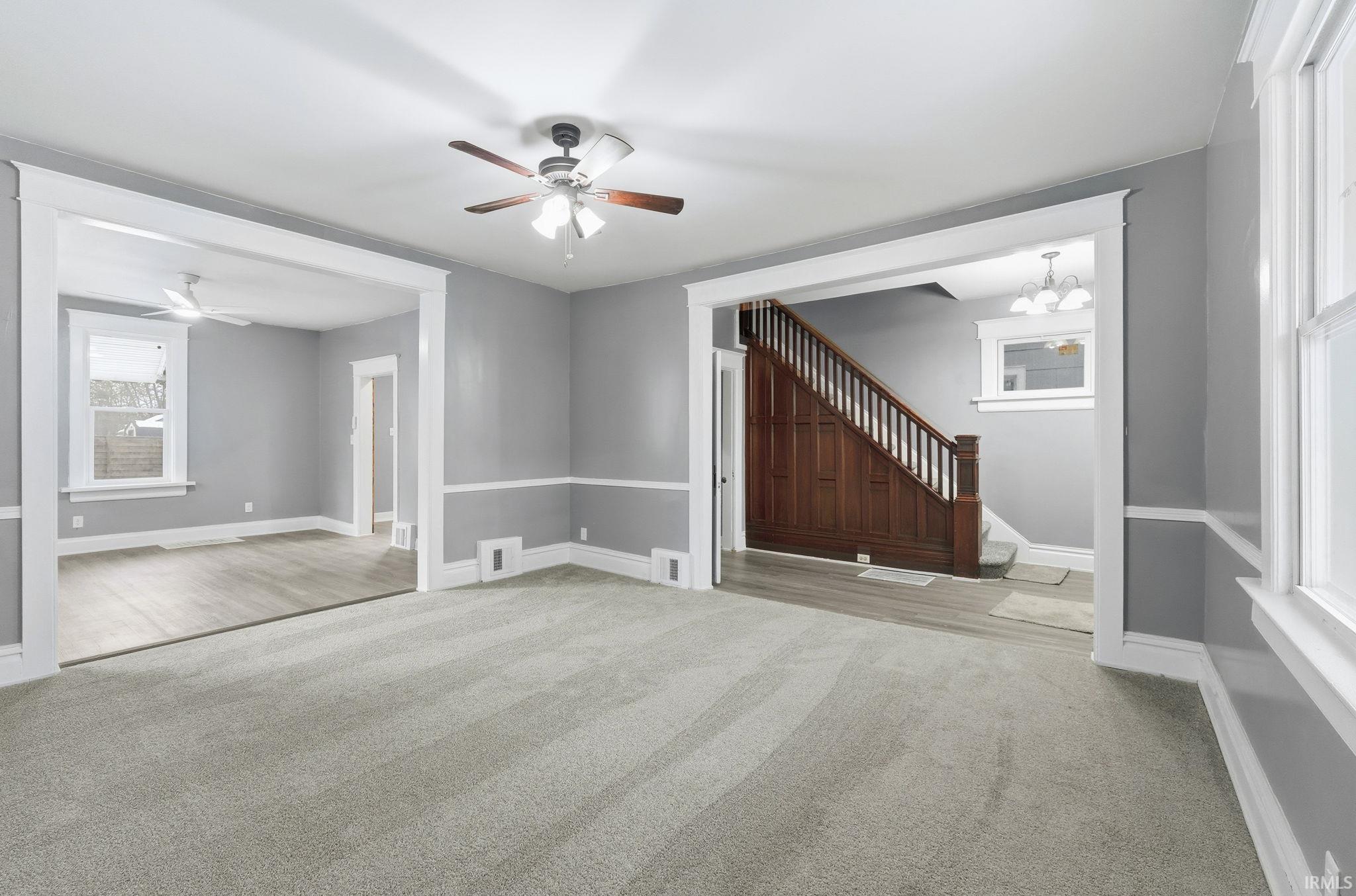 Unfurnished living room featuring a ceiling fan, light carpet, stairway, and a chandelier