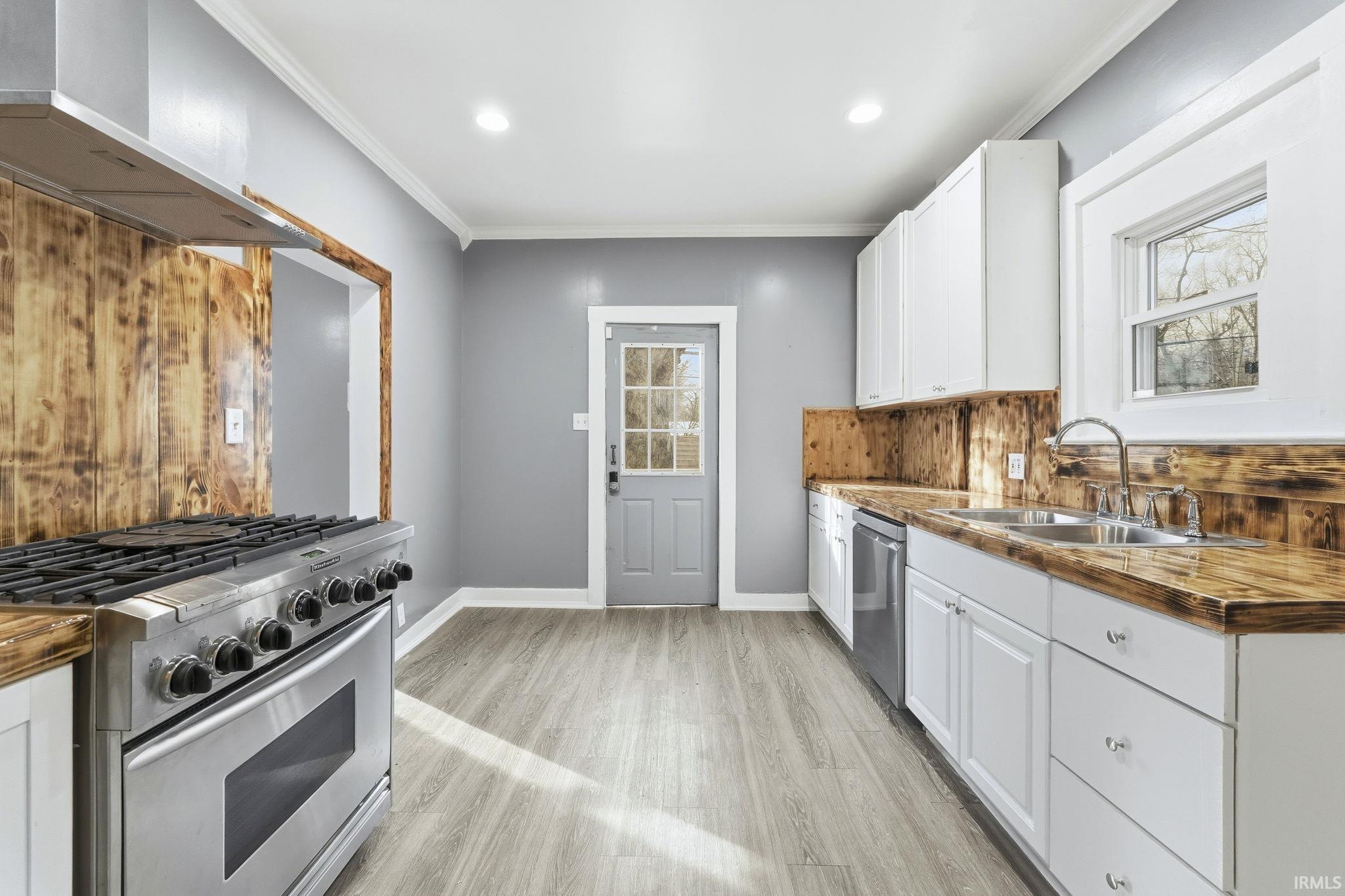 Kitchen featuring stainless steel appliances, white cabinets, crown molding, wall chimney exhaust hood, and wooden counters