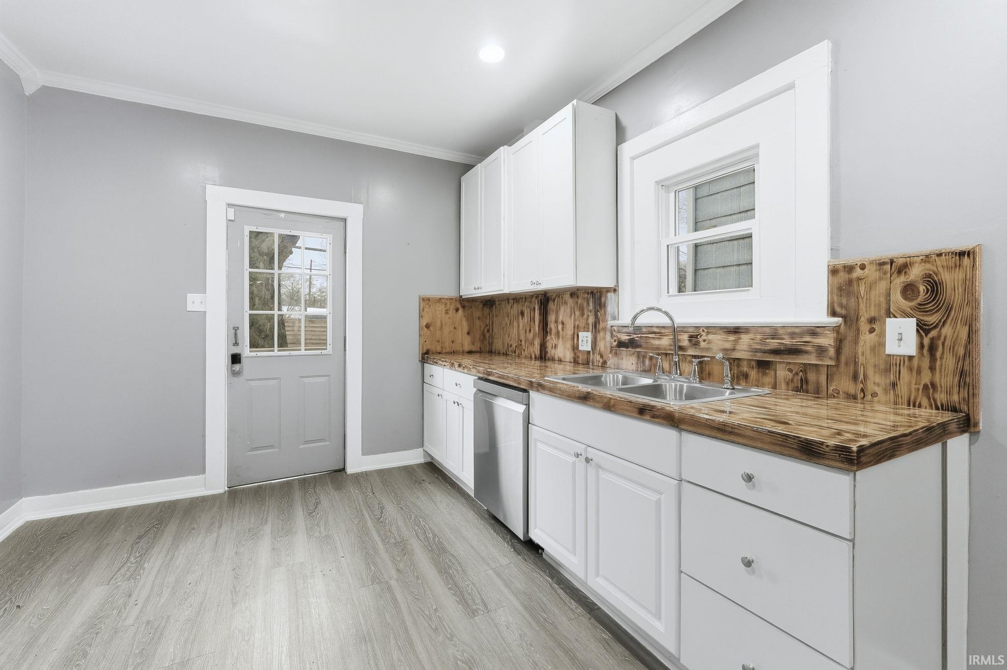 Kitchen featuring white cabinets, ornamental molding, dishwasher, light wood finished floors, and dark countertops