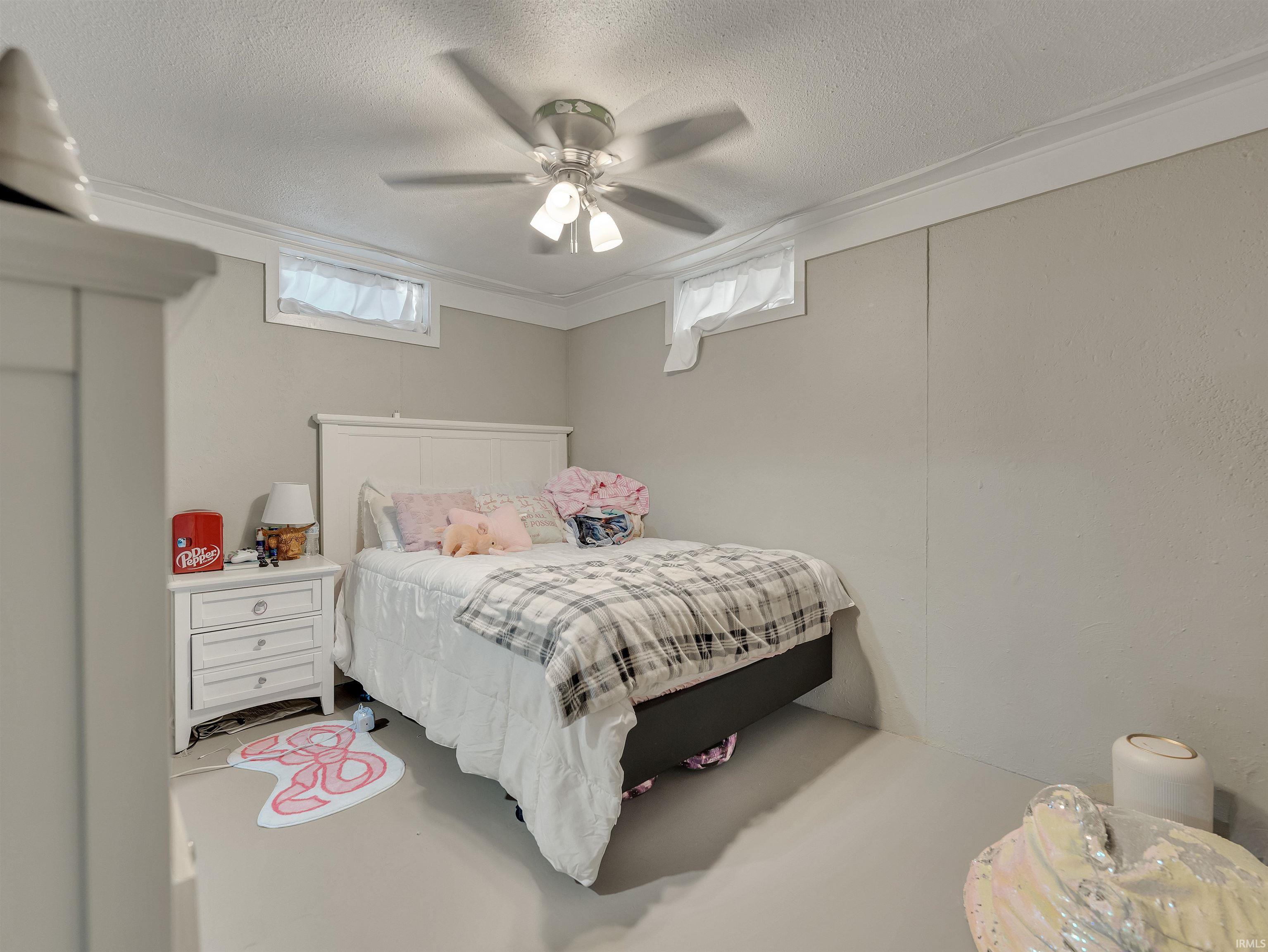 Bedroom featuring a textured ceiling, multiple windows, ceiling fan, and finished concrete flooring