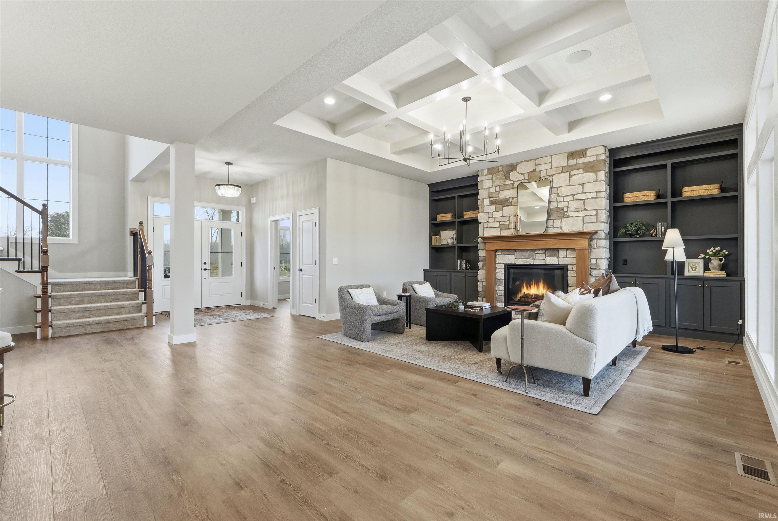 Living room featuring stairway, coffered ceiling, built in shelves, a fireplace, and light wood-style floors