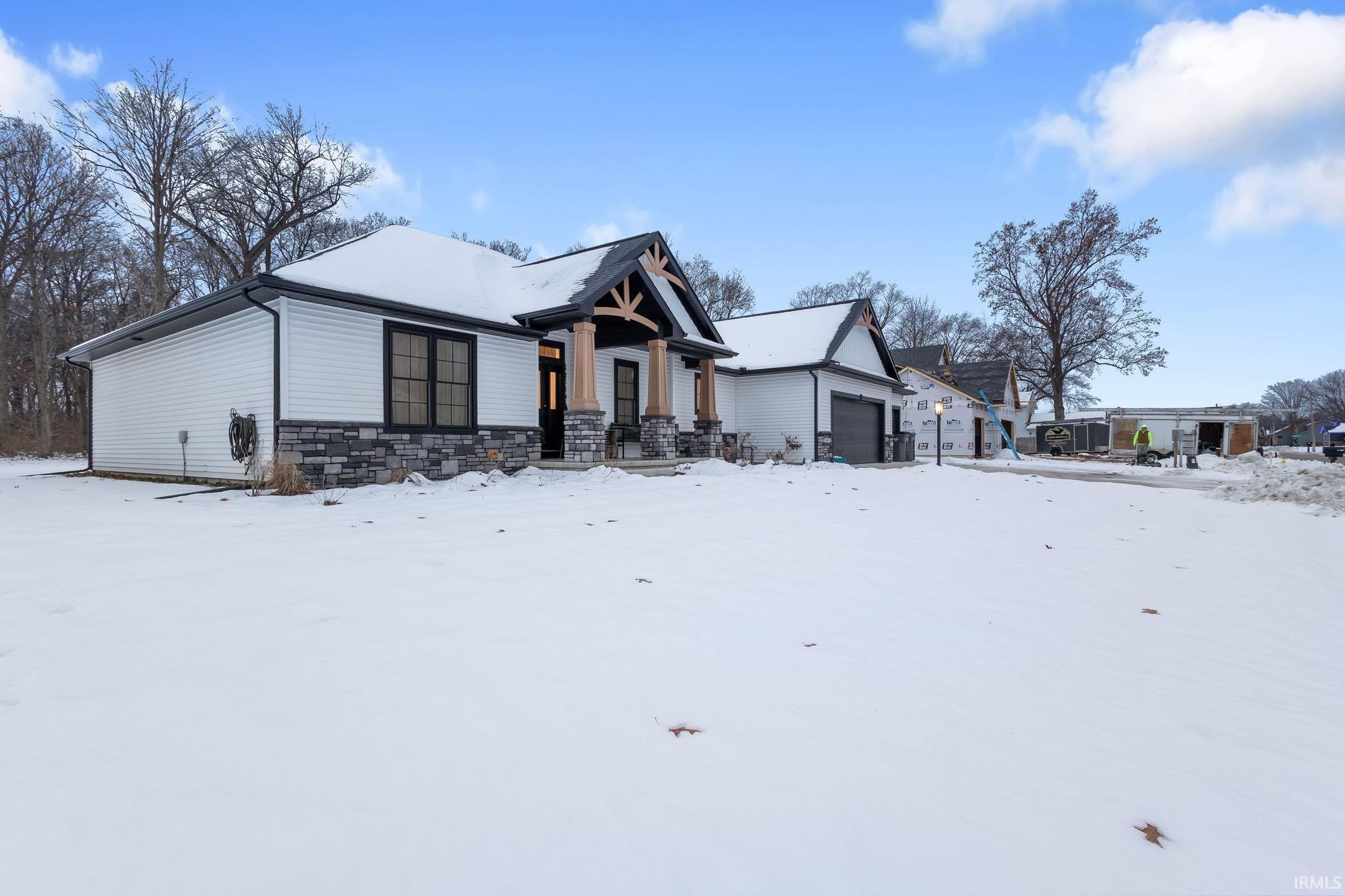 View of snow covered exterior with an attached garage and stone siding